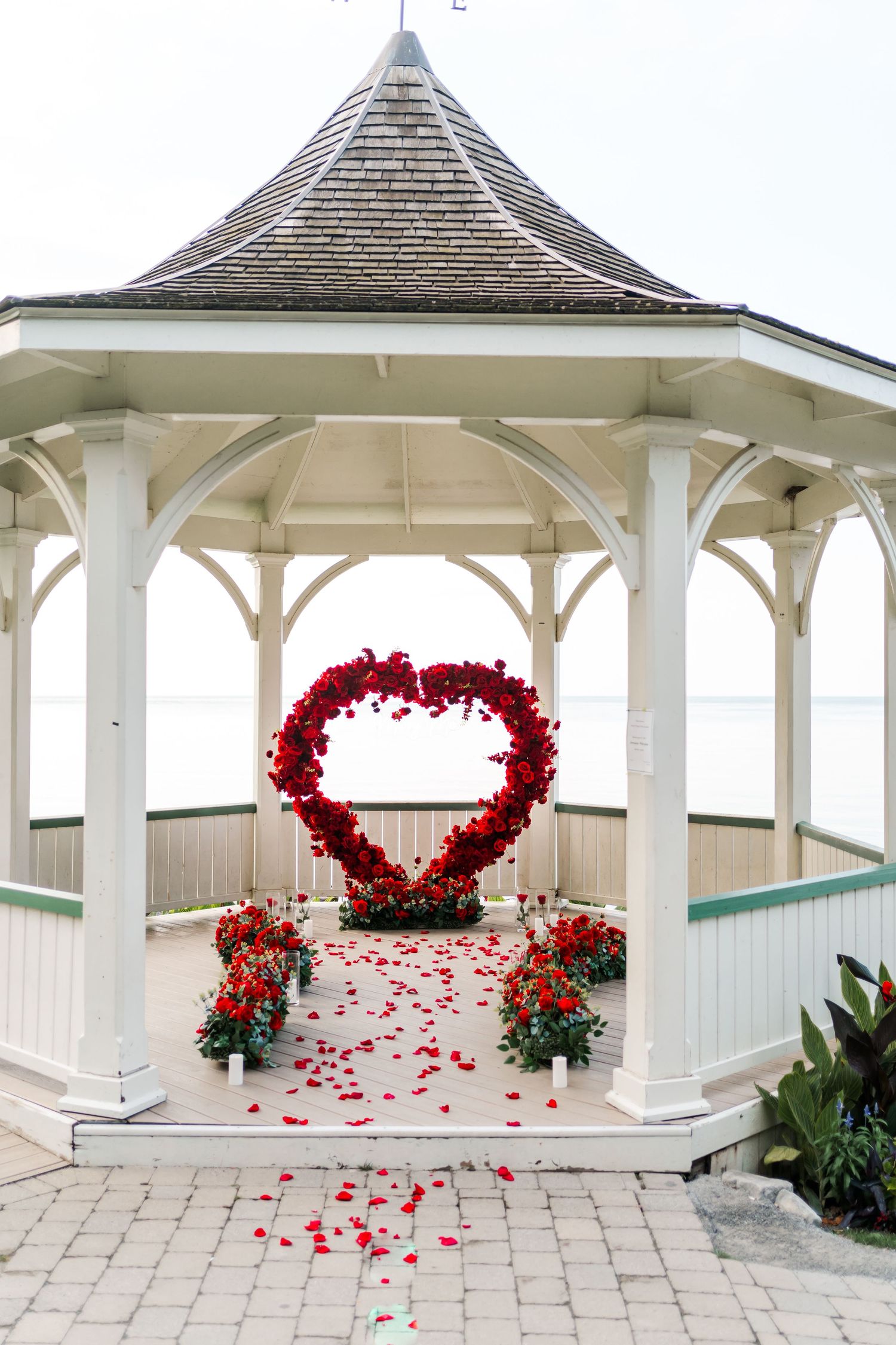 White gazebo decorated with large red heart-shaped floral arch and rose petals.
Niagara Proposal.