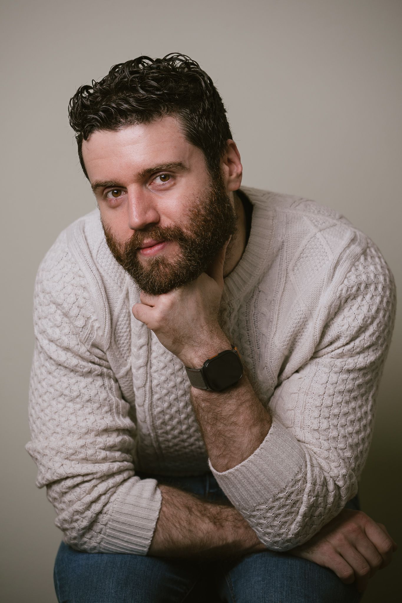White man, clothed, seated in studio light, part of a portrait series exploring masculinity and body‑positive representation.