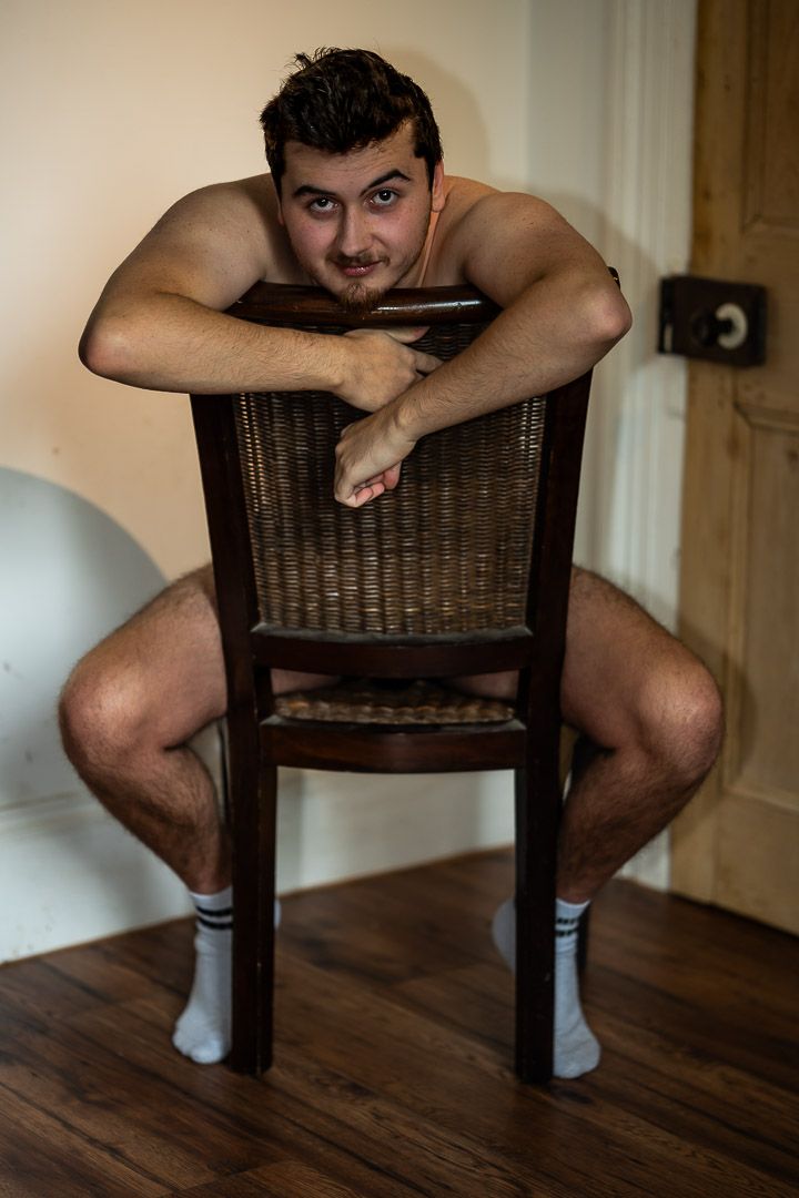 White man, naked, seated in natural light, part of a portrait series exploring masculinity and body‑positive representation.