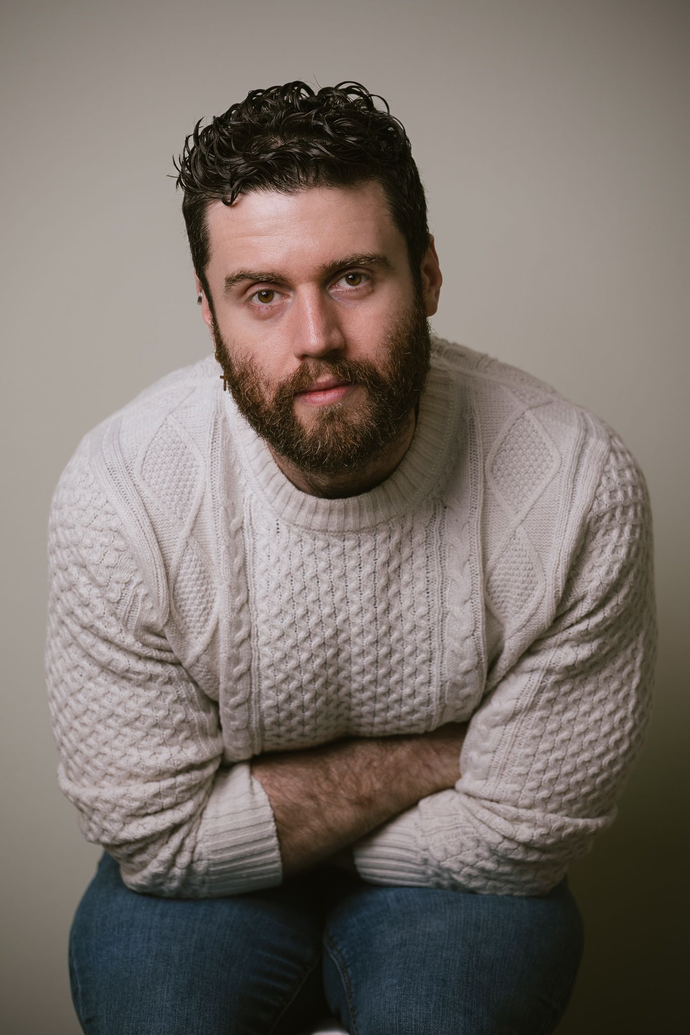 White man, clothed, seated in studio light, part of a portrait series exploring masculinity and body‑positive representation.