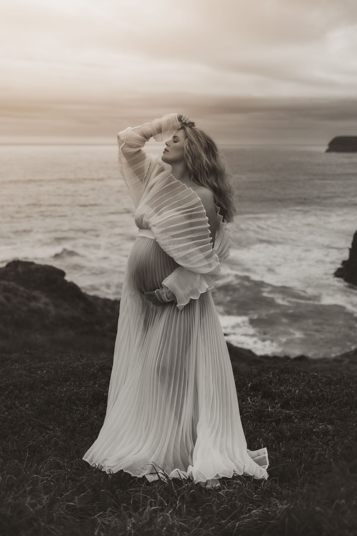 A dreamy coastal portrait showcases a flowing white dress against ocean cliffs.