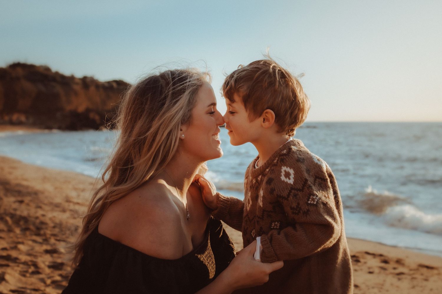 Romantic couple embracing on a beach at golden hour with ocean waves in the background.