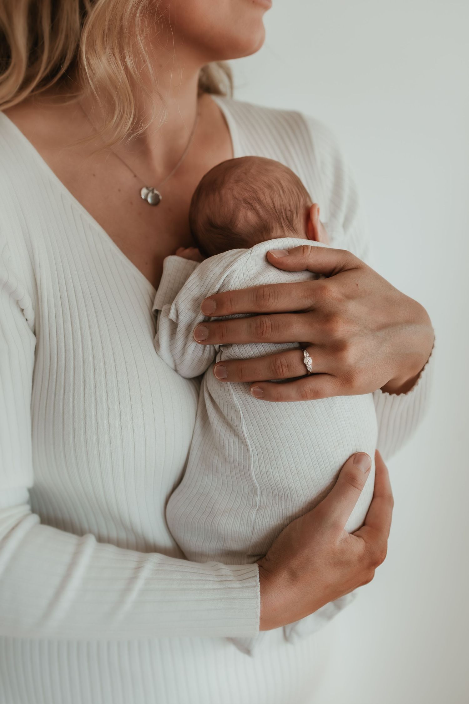 A series of intimate photos showing hands gently cradling a newborn baby against a white sweater.