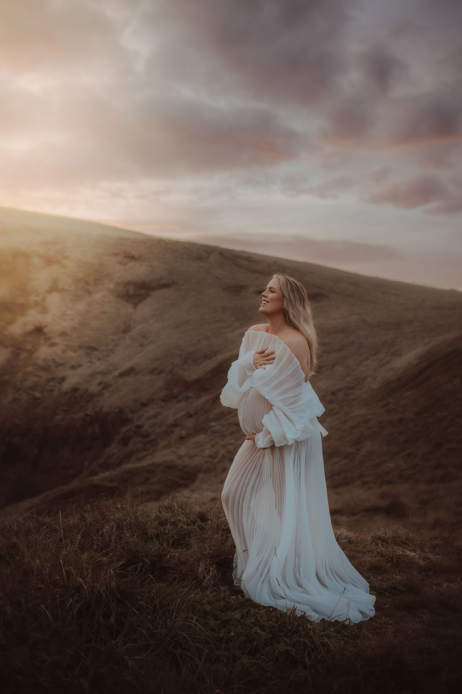 A flowing white dress stands out against rolling hills during golden hour.