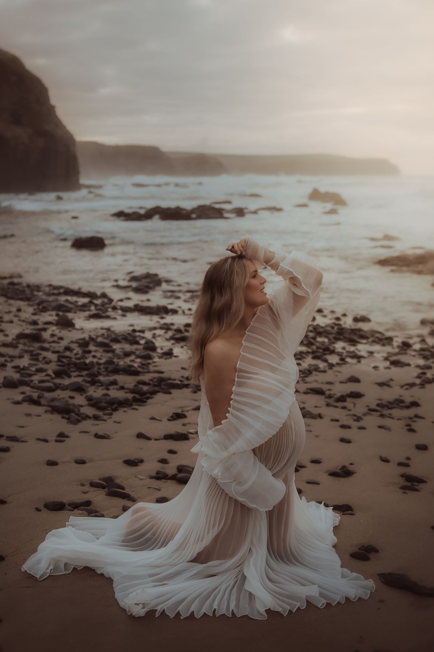 Ethereal white dress movement captured on rocky beach at sunset.
