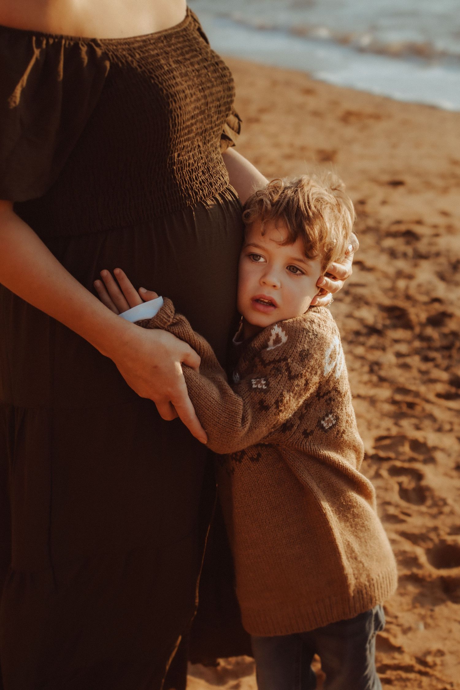 Close-up shots of a toddler in a brown sweater on the beach.
