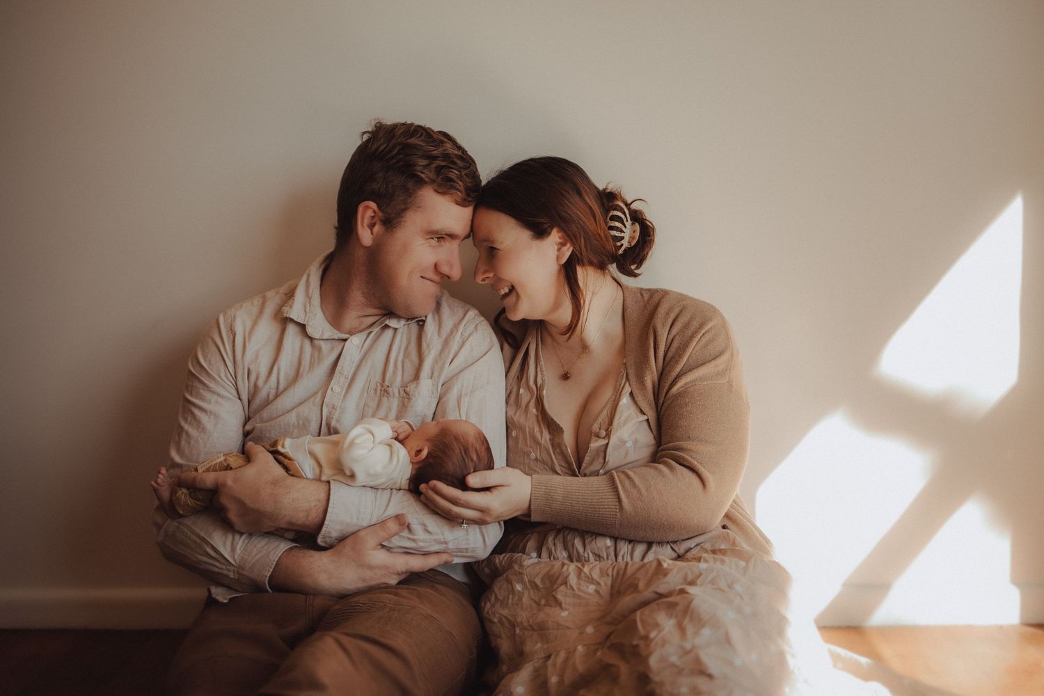 Intimate family moment with newborn baby in warm natural window light.