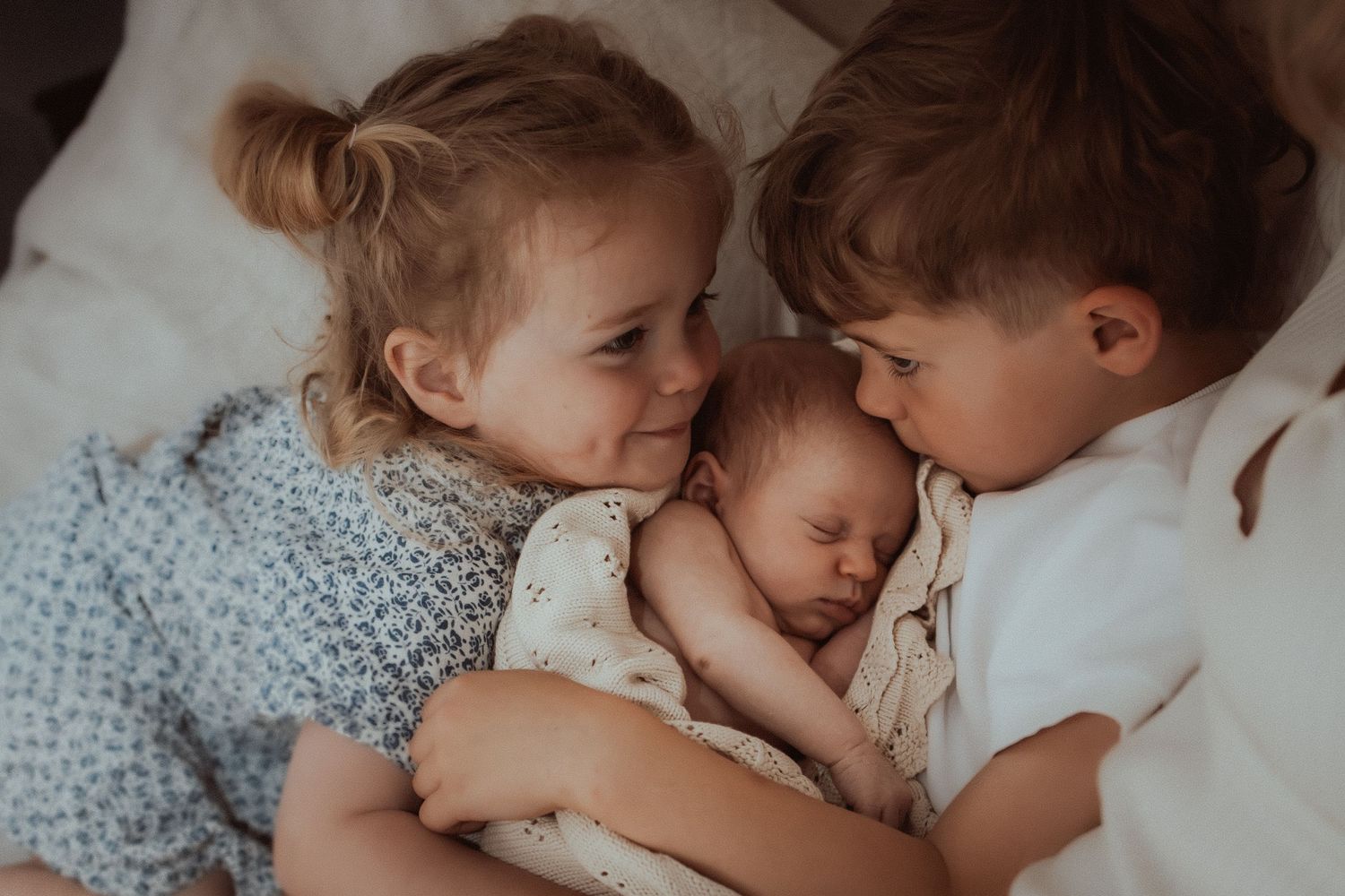 Two small children lie peacefully sleeping together on white bedding in a tender moment.