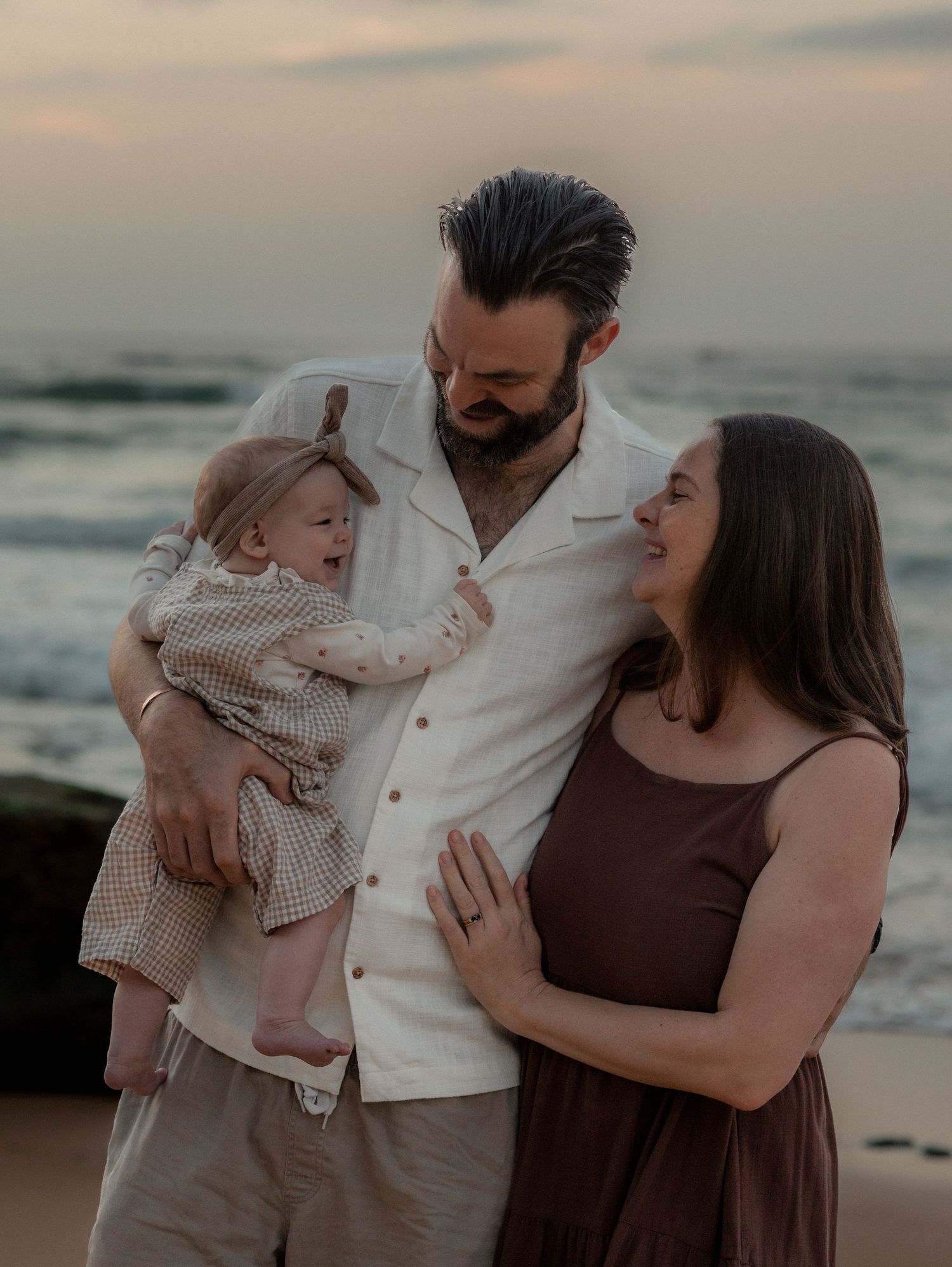 A family shares tender moments together on a beach at sunset in a series of candid photographs.