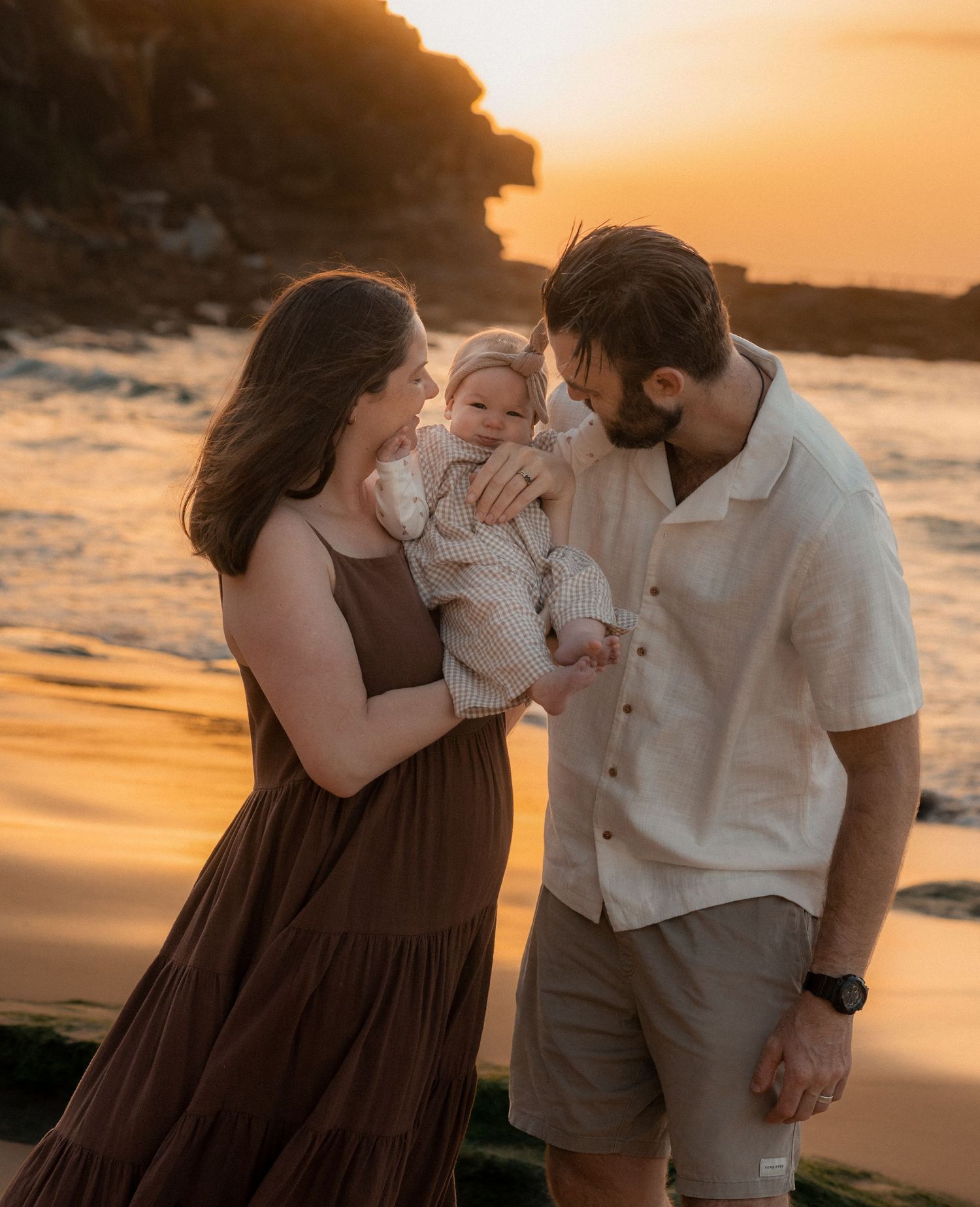 A family shares tender moments together on a beach at sunset with warm golden light illuminating their silhouettes.