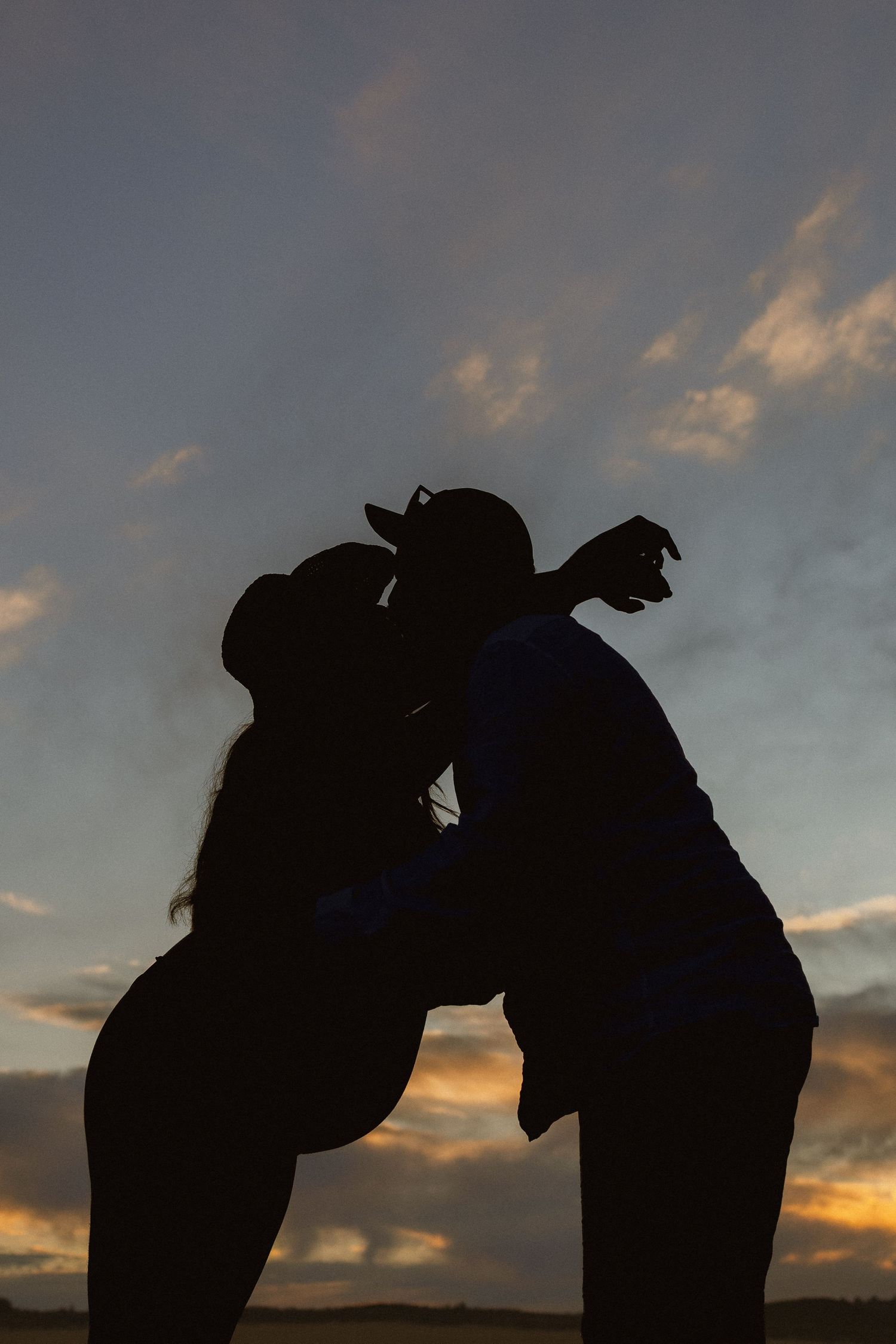 Silhouette of a couple kissing at sunset with dramatic cloudy sky in the background.