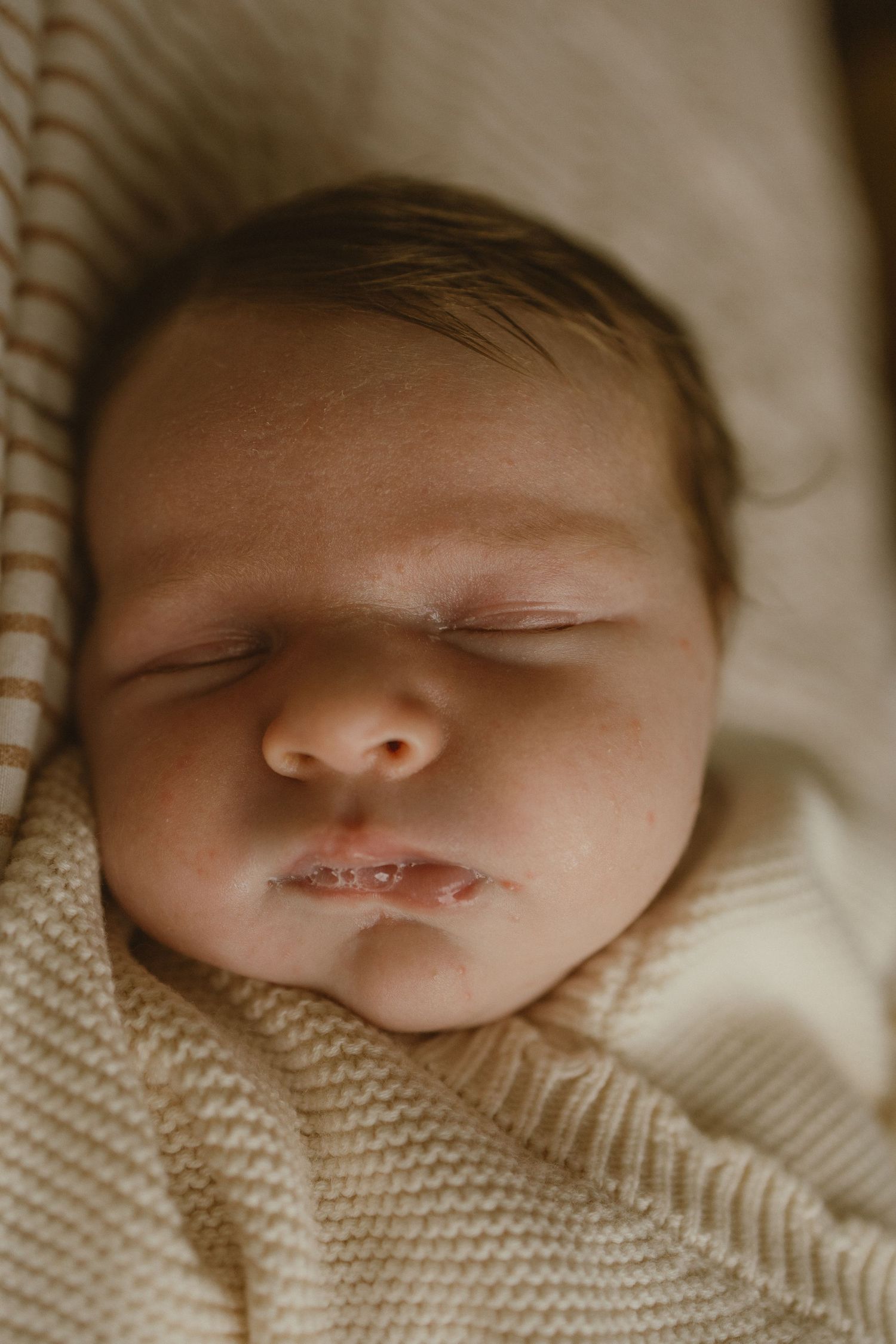 Close-up of a peaceful sleeping newborn baby wrapped in a soft cream knit blanket.