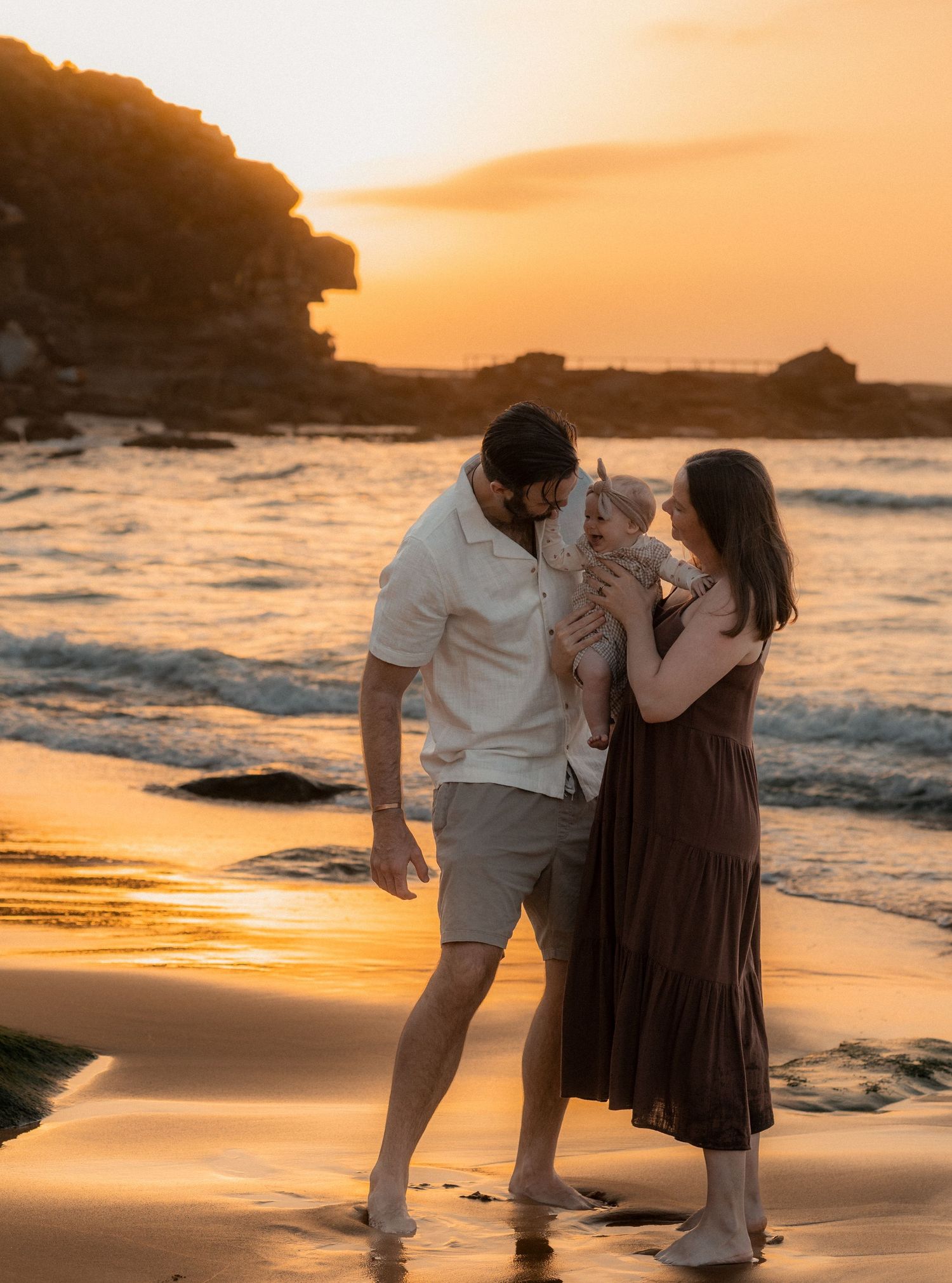 A family enjoys a sunset moment together on a beach with rocky cliffs.
