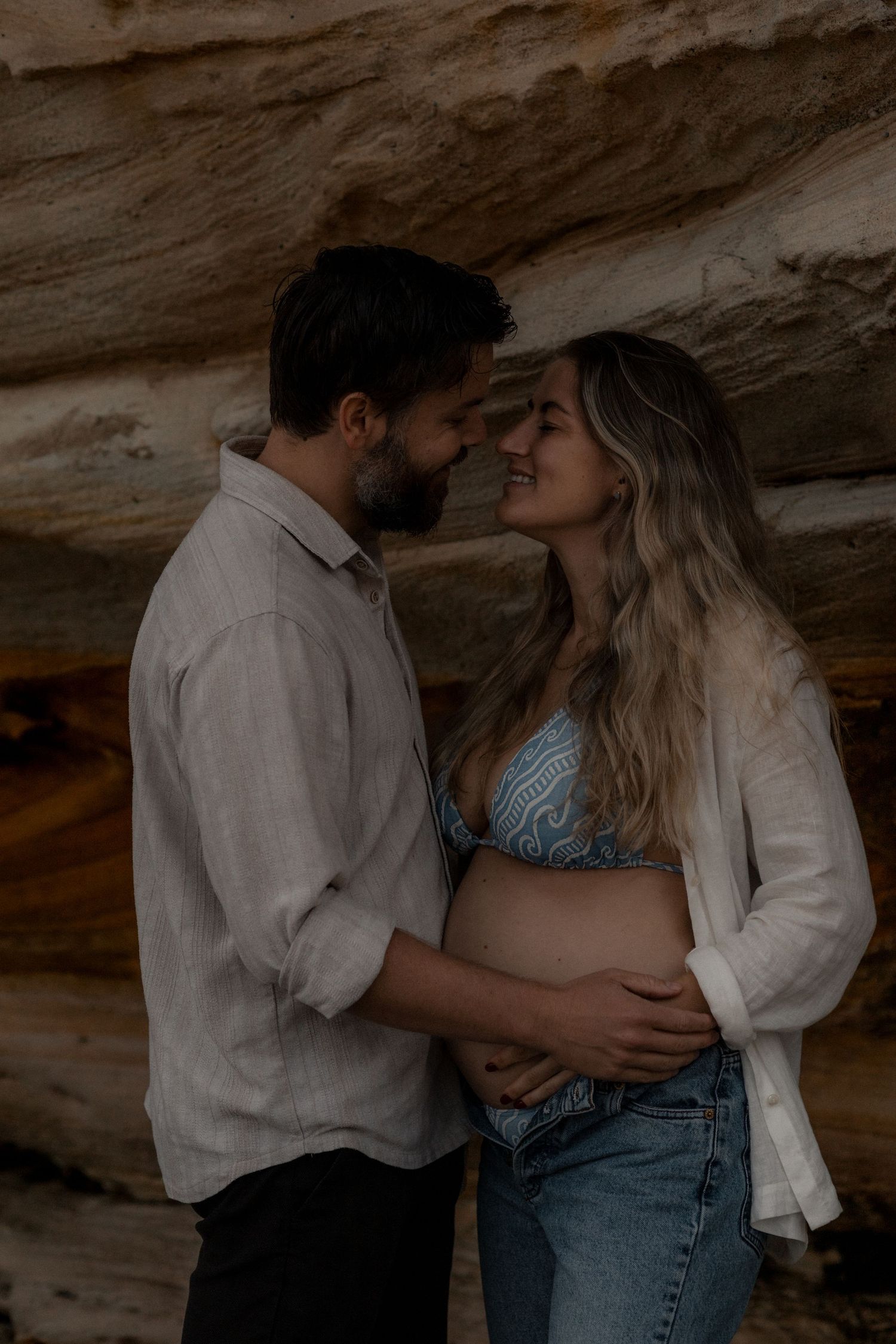 A couple shares an intimate moment against a rocky cliff backdrop.