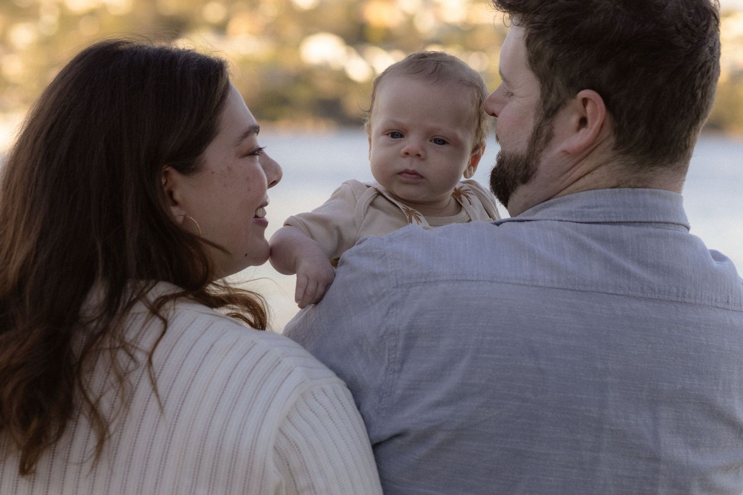 A couple sharing a tender moment with their baby outdoors in soft golden light.