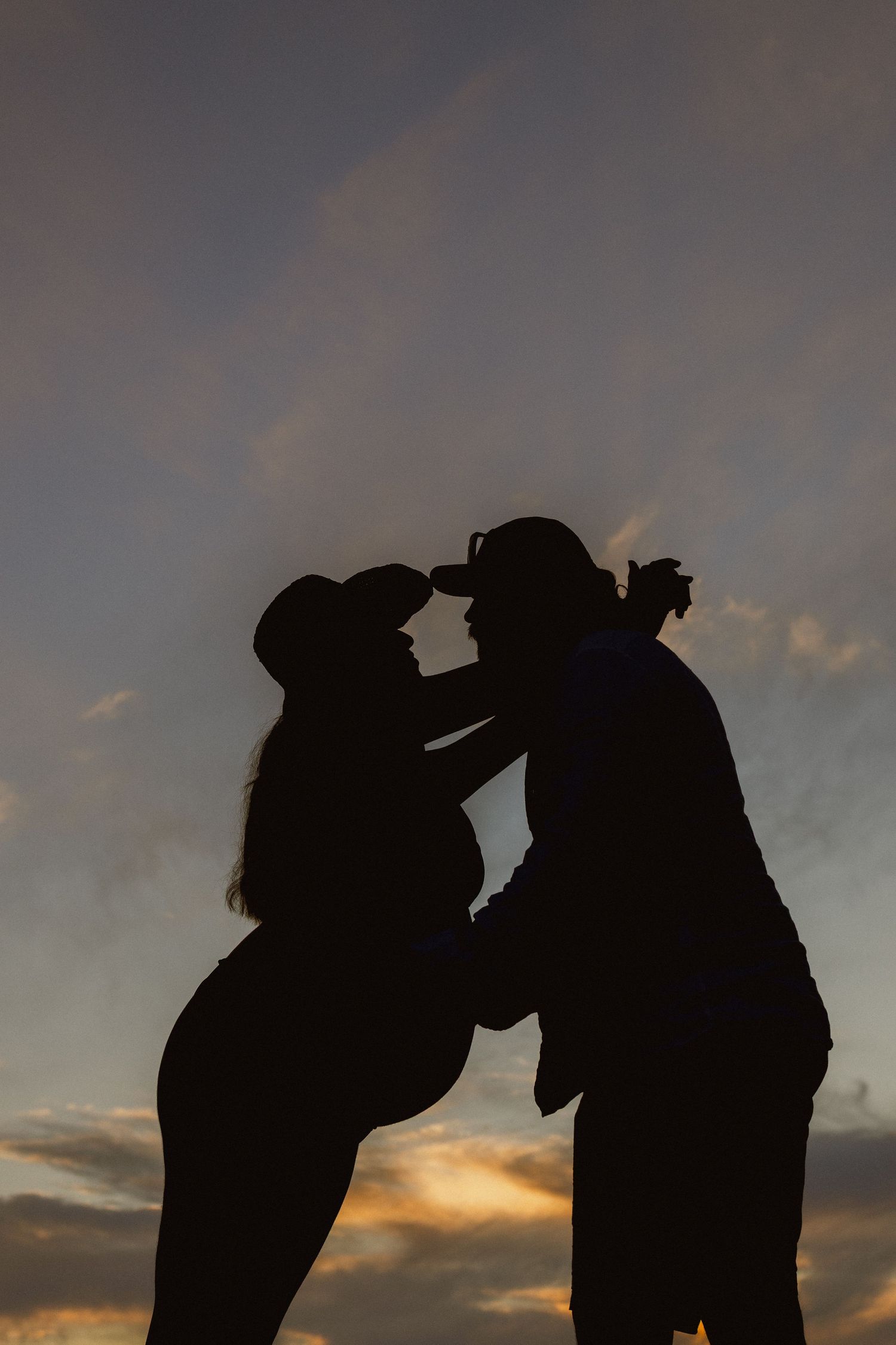 Romantic silhouette of a couple about to kiss against a dramatic sunset sky with clouds.