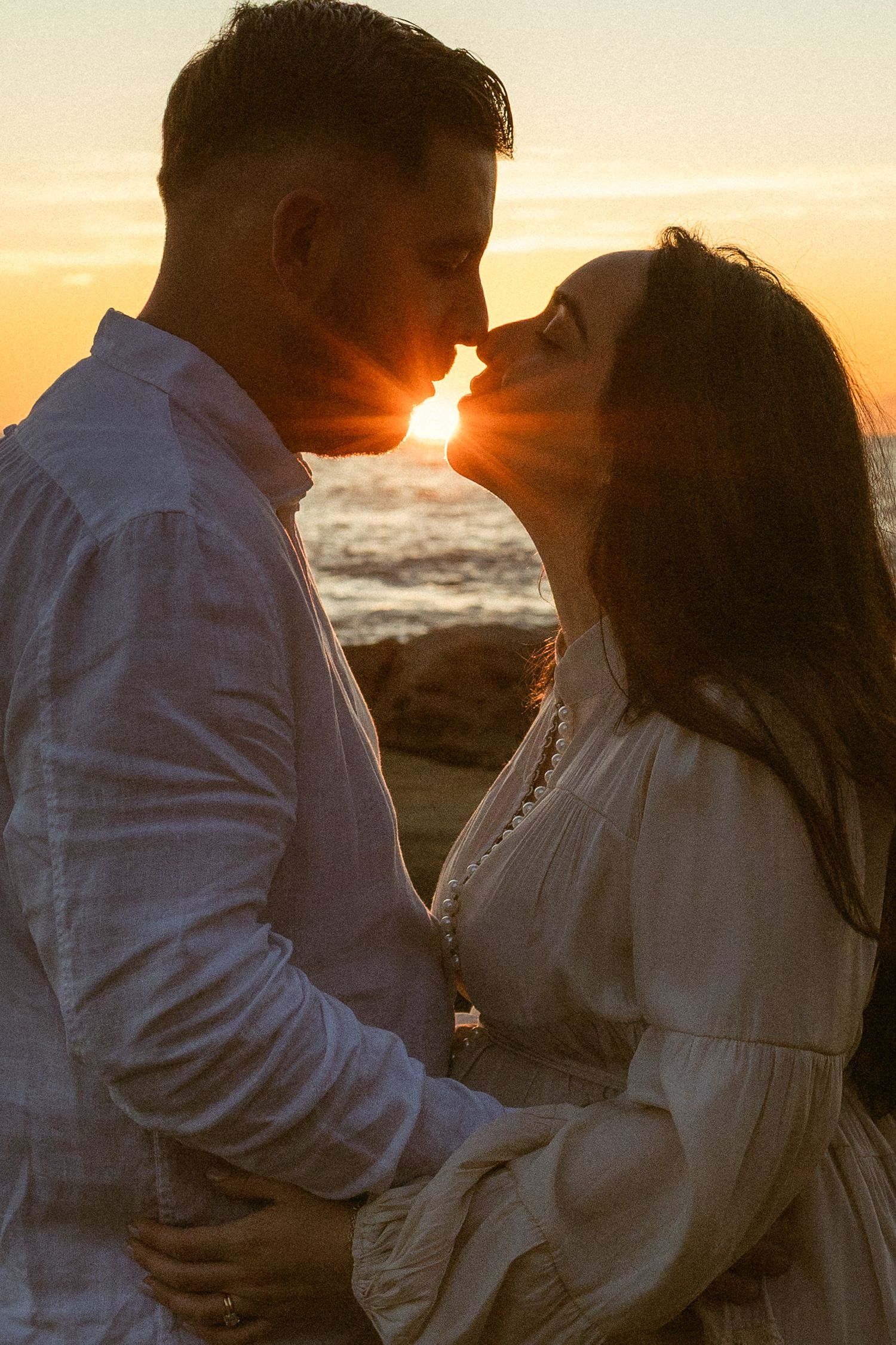 Couple sharing a romantic kiss at sunset on the beach, golden light glowing between them.