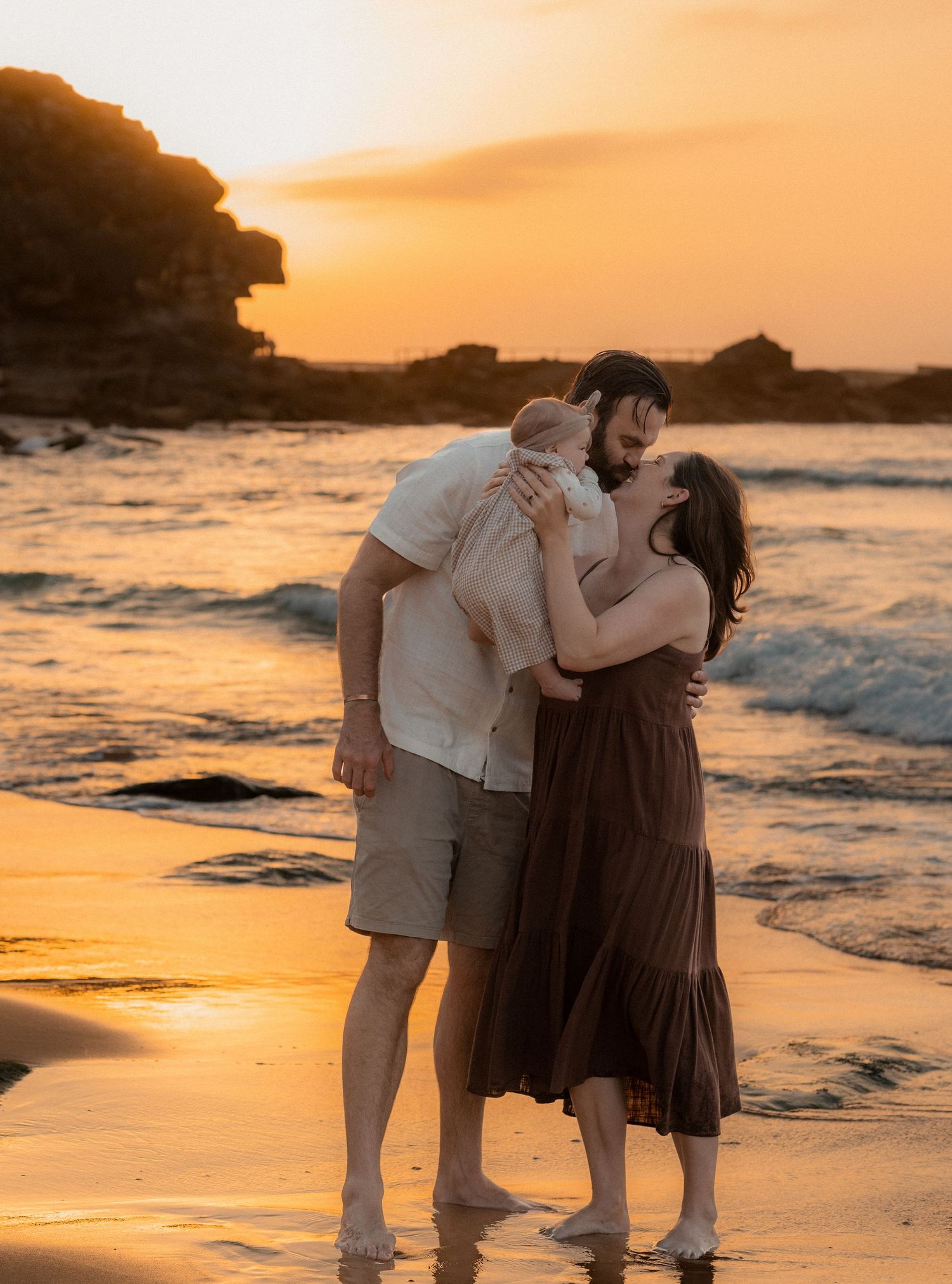 Couple sharing intimate moments on a beach at golden hour with dramatic coastal scenery.