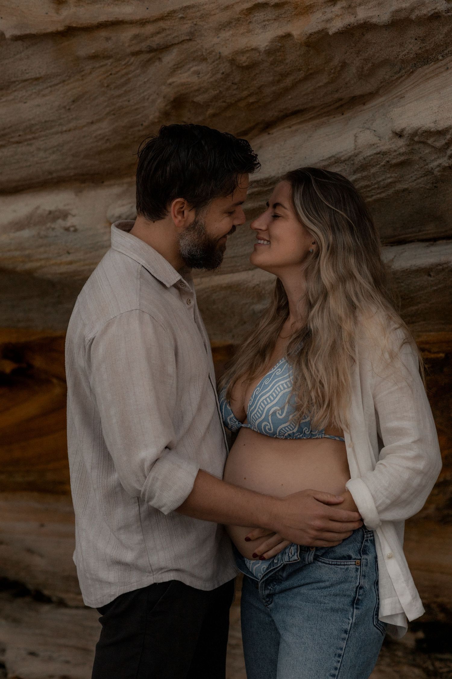 A romantic couple shares intimate moments in a cave-like setting with natural rock formations in the background.
