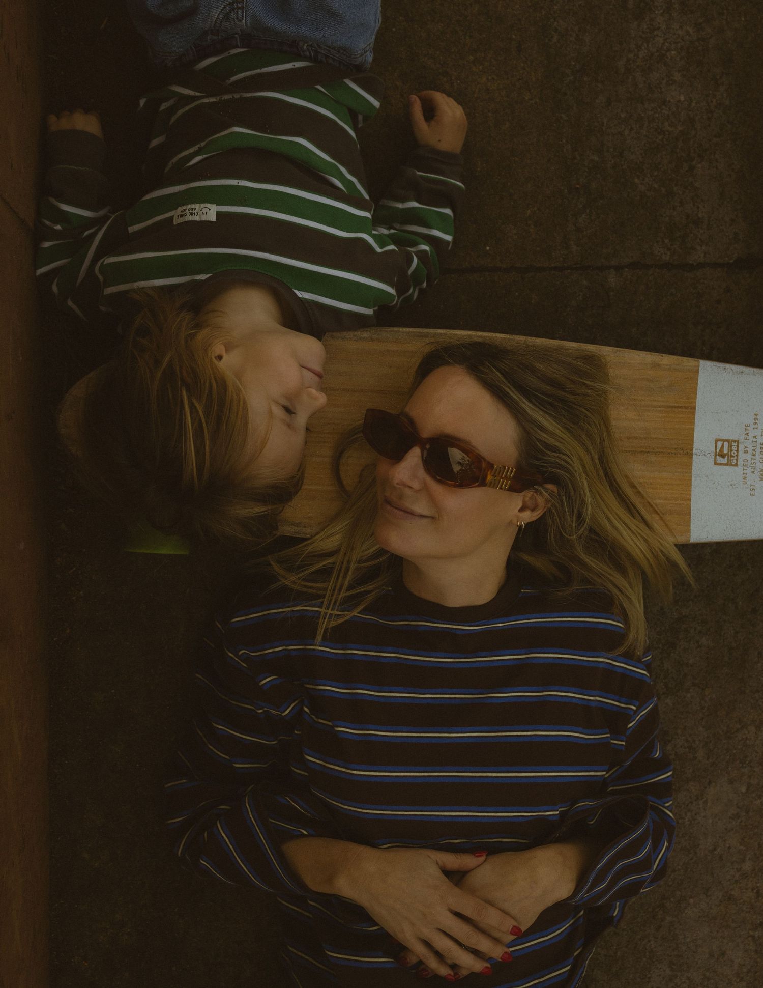 A woman and child lying on the floor smiling, wearing striped shirts, the woman in sunglasses.