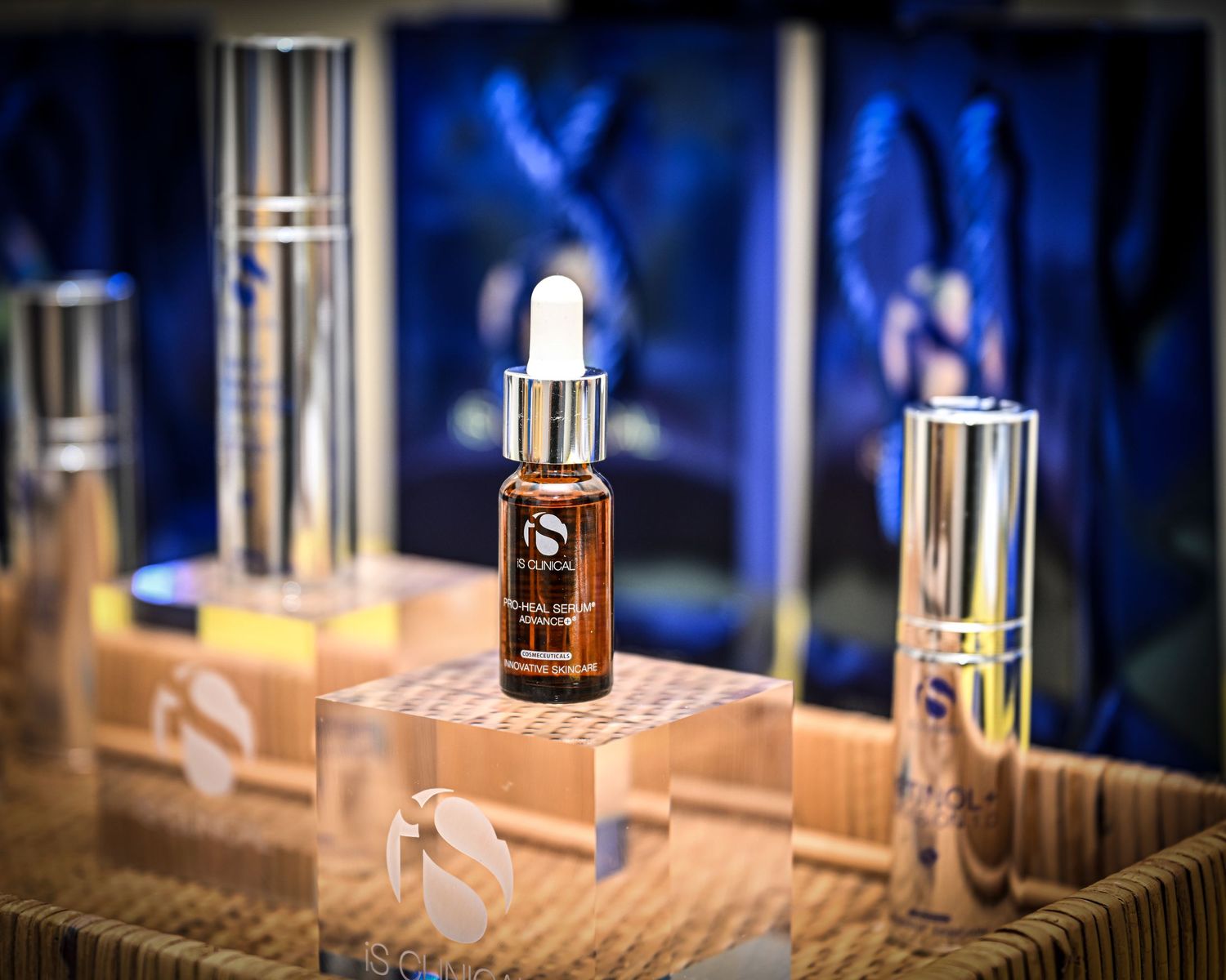 iS Clinical skincare products displayed on wooden risers, featuring a serum dropper bottle and luxury cosmetic containers.