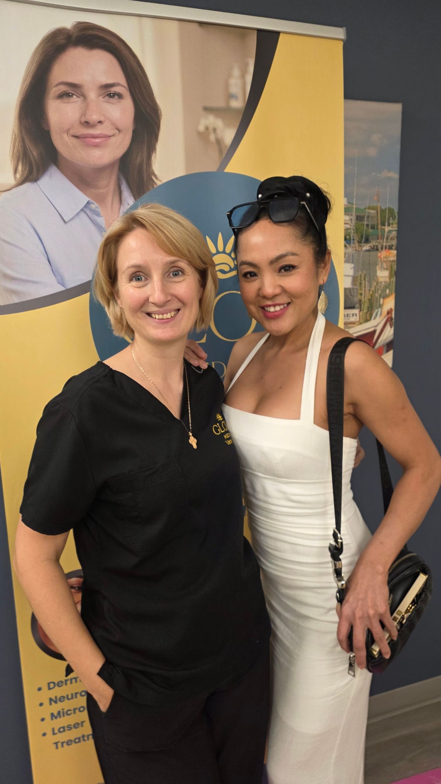 Two women pose together in front of a medical spa banner offering dermatology and laser treatments.