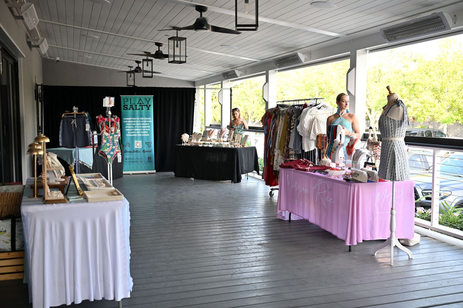 Outdoor boutique pop-up shop displaying clothing on mannequins and racks on a covered wooden deck patio.