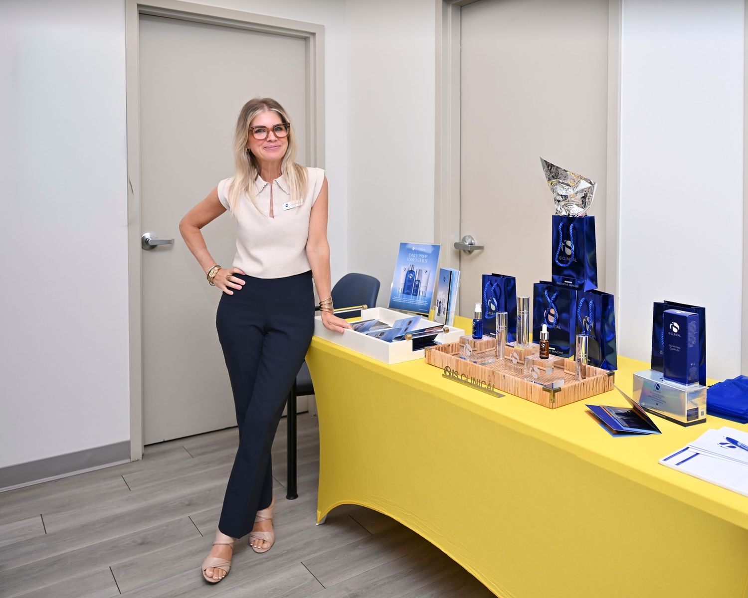 Woman standing beside a yellow table displaying blue crystal awards and trophies in a modern office setting.