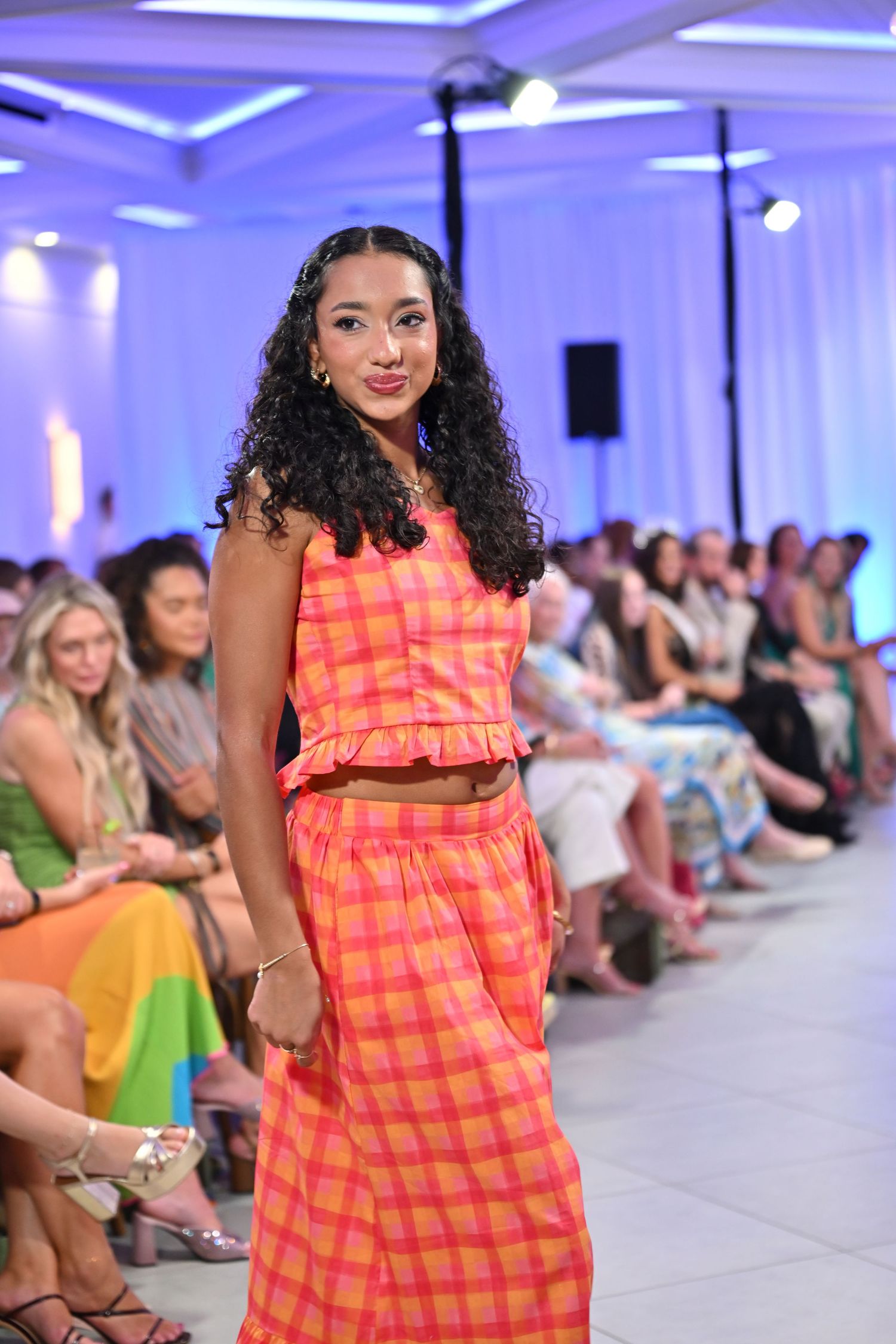 Model walks runway in orange and pink plaid crop top and maxi skirt set at a fashion show.