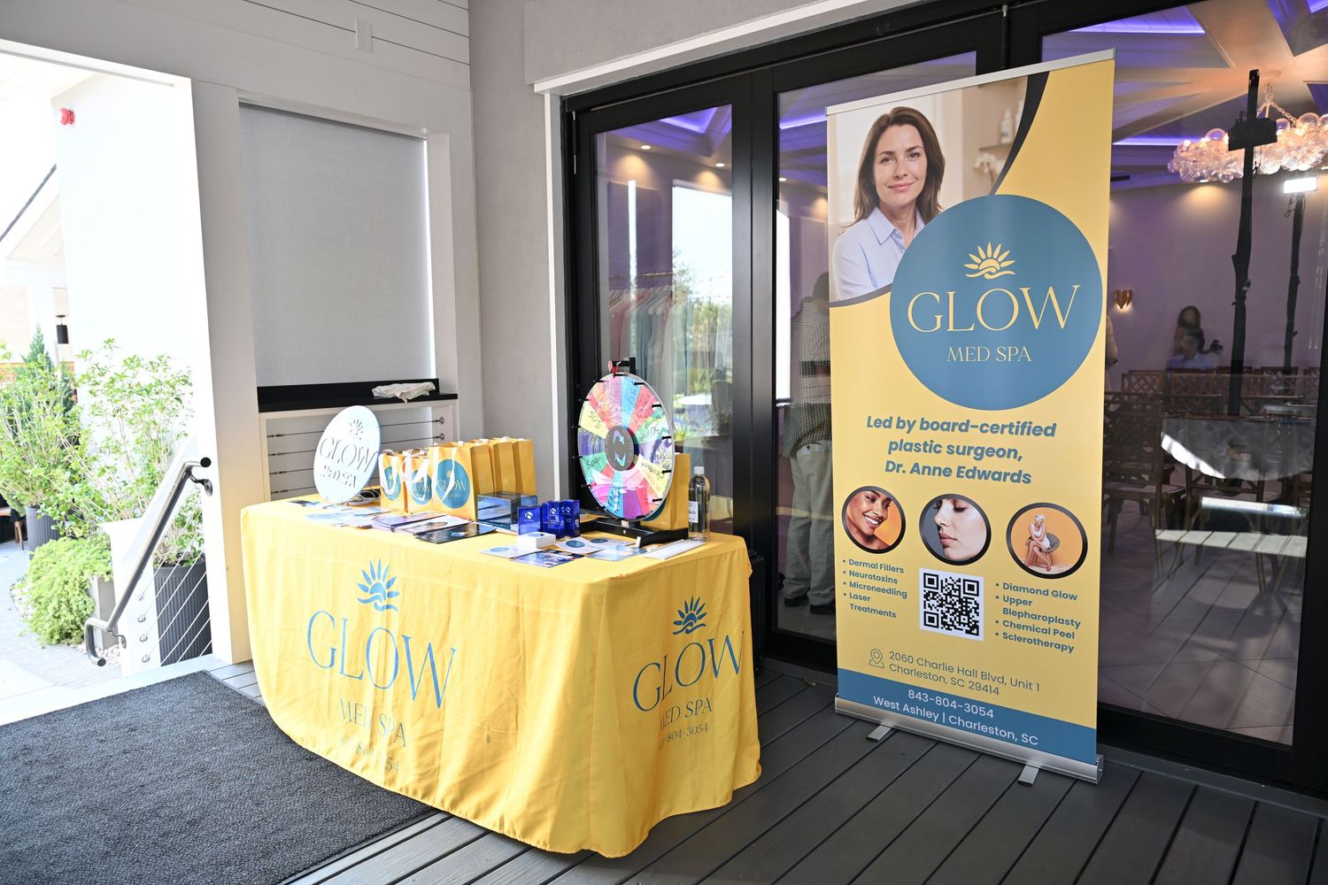 Glow plastic surgery booth with yellow tablecloth, promotional banner featuring Dr. Jesse, and prize wheel at an outdoor event.