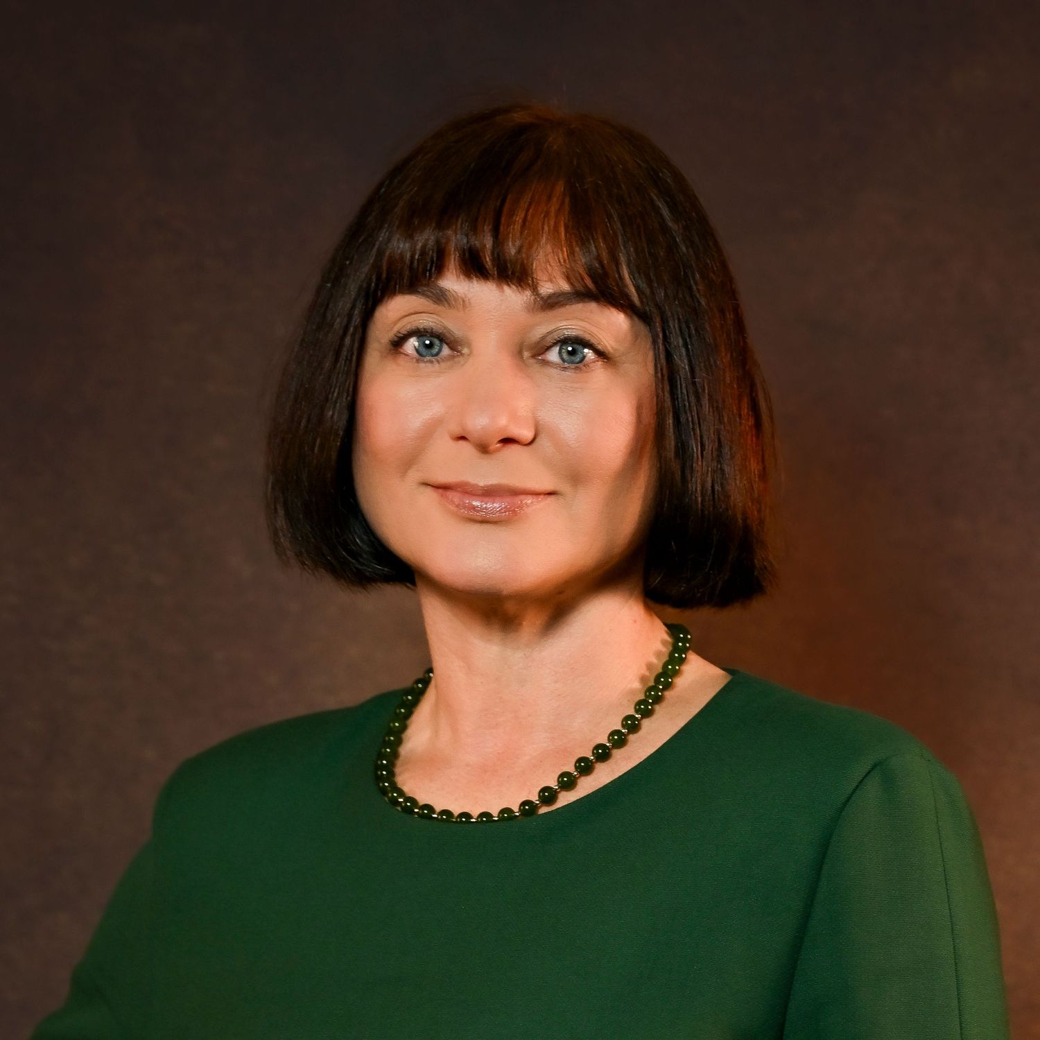 Professional woman with a dark bob haircut wearing a green blouse and pearl necklace poses for a portrait.