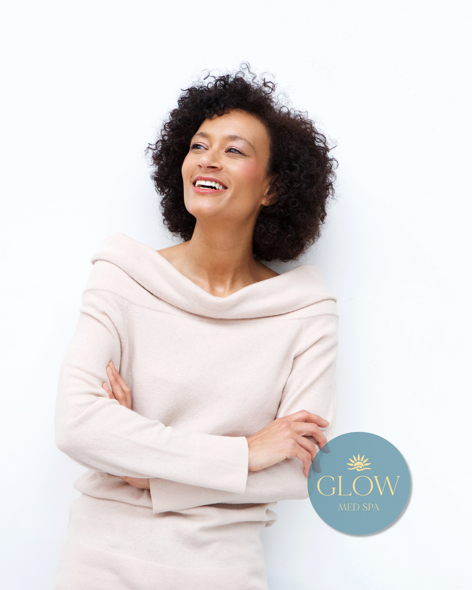 Happy woman with curly hair and crossed arms smiling brightly with Glow Med Spa branding.
