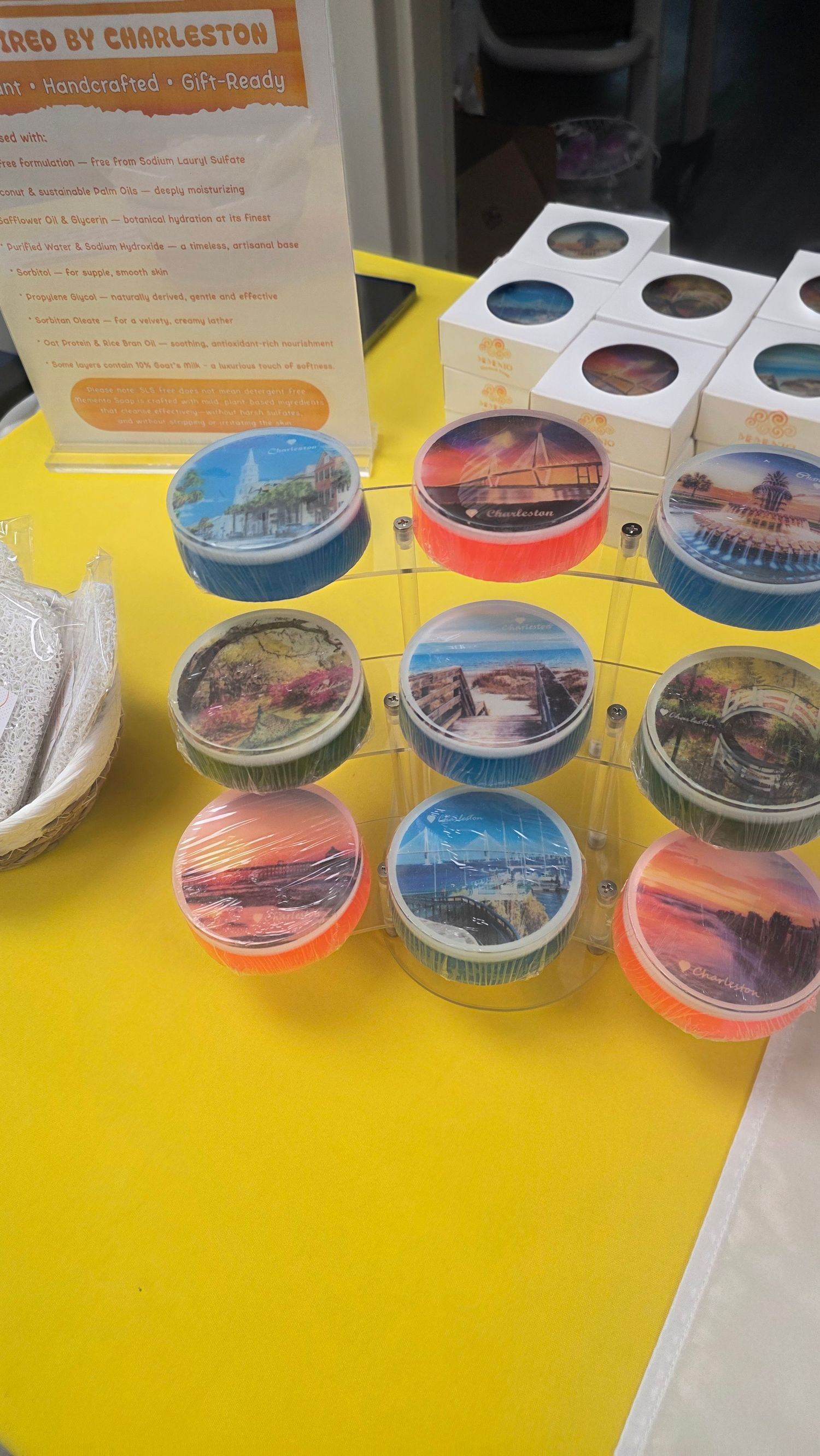 Colorful Charleston-themed souvenir candle tins with scenic photo lids displayed on a bright yellow table at a gift shop.