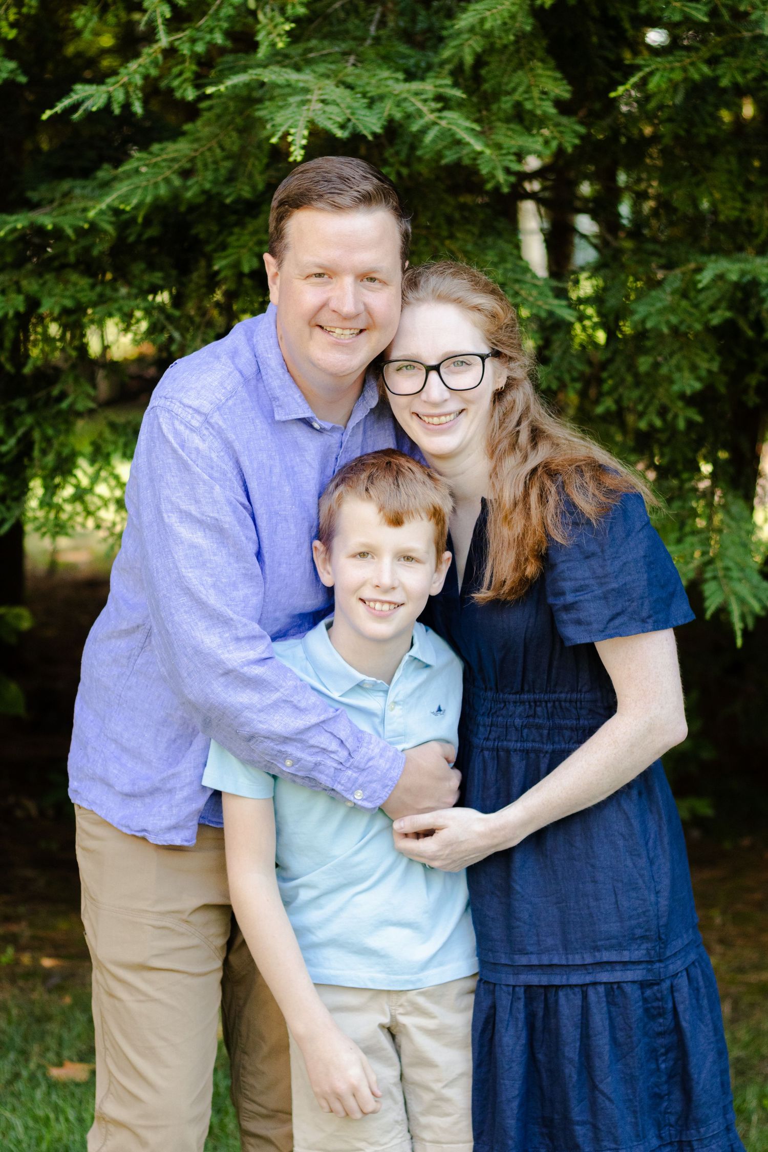 A family of three poses together outdoors against a leafy green background in a series of candid moments.