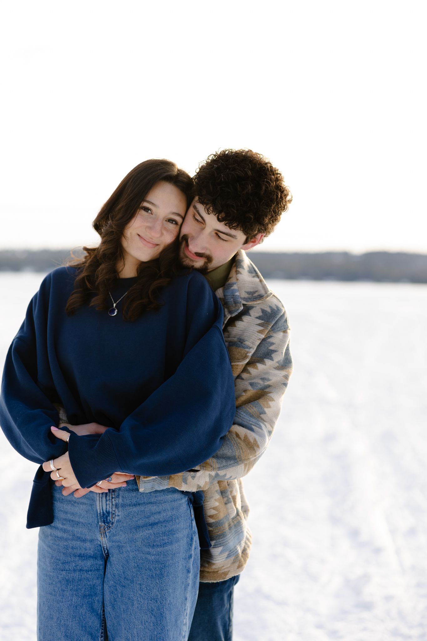 Winter scene with two people embracing in front of a snowy landscape.