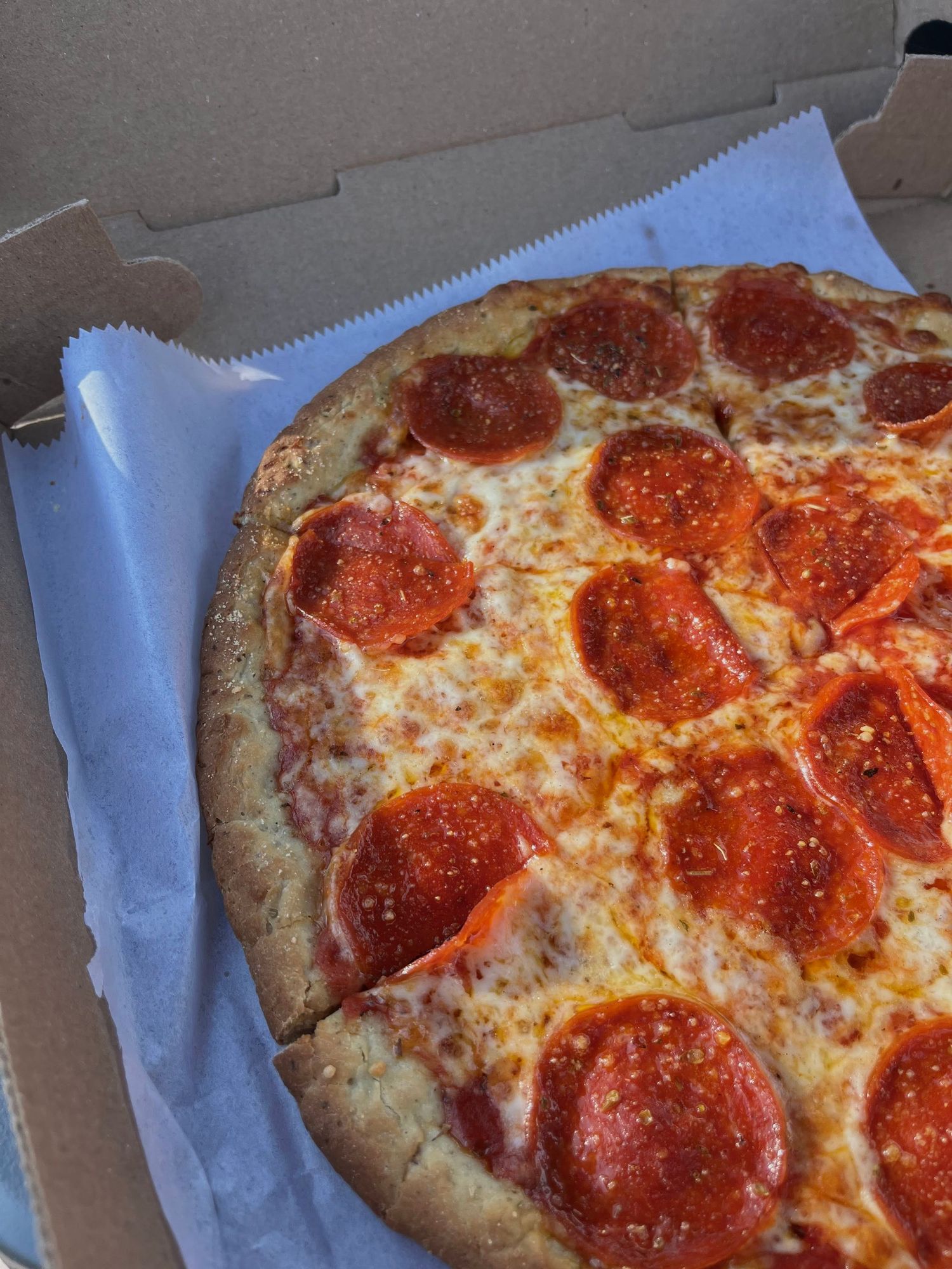 A pepperoni pizza with melted cheese in a cardboard delivery box.