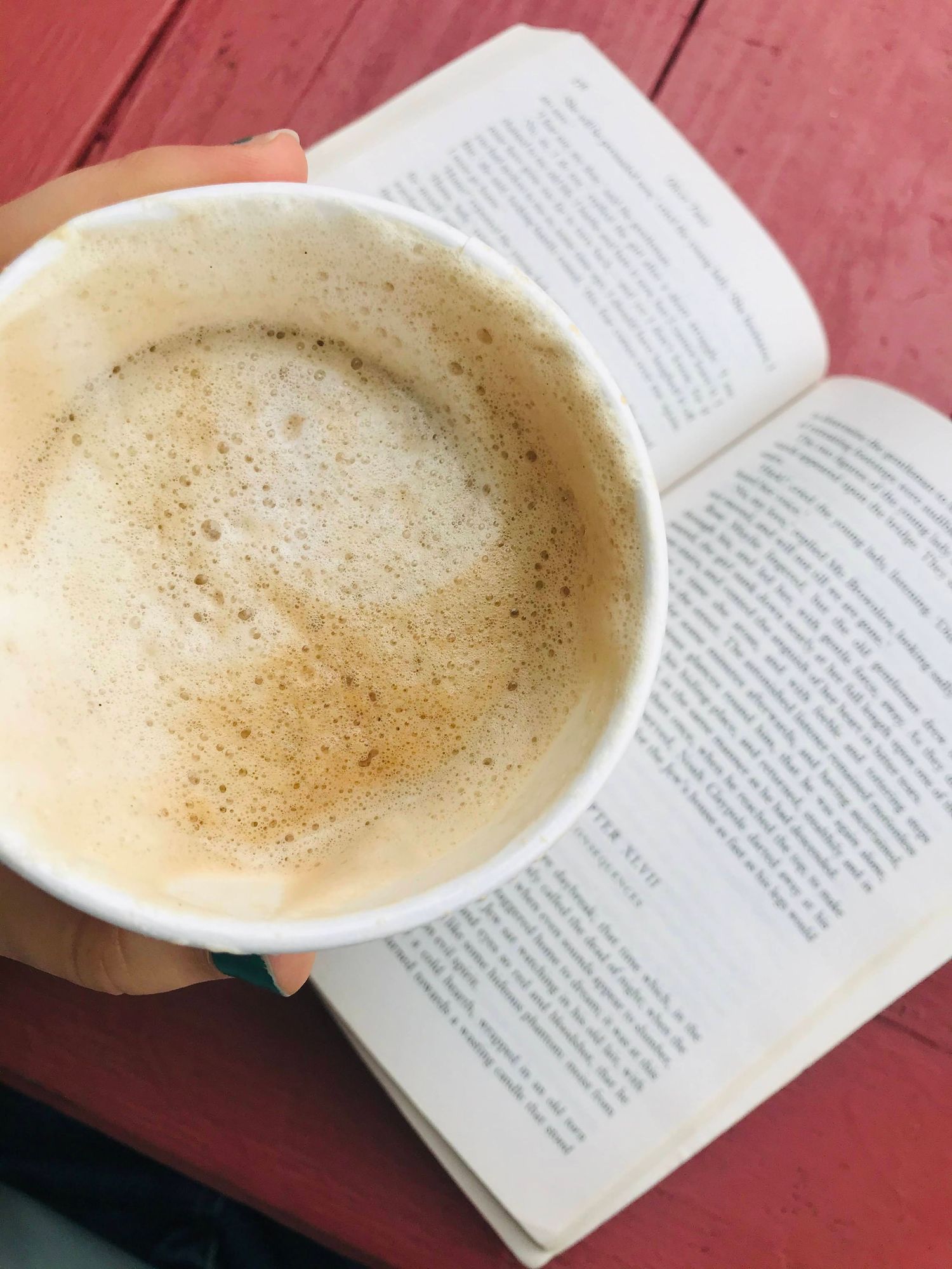 Coffee cup with frothy foam resting on an open book on a red wooden surface.