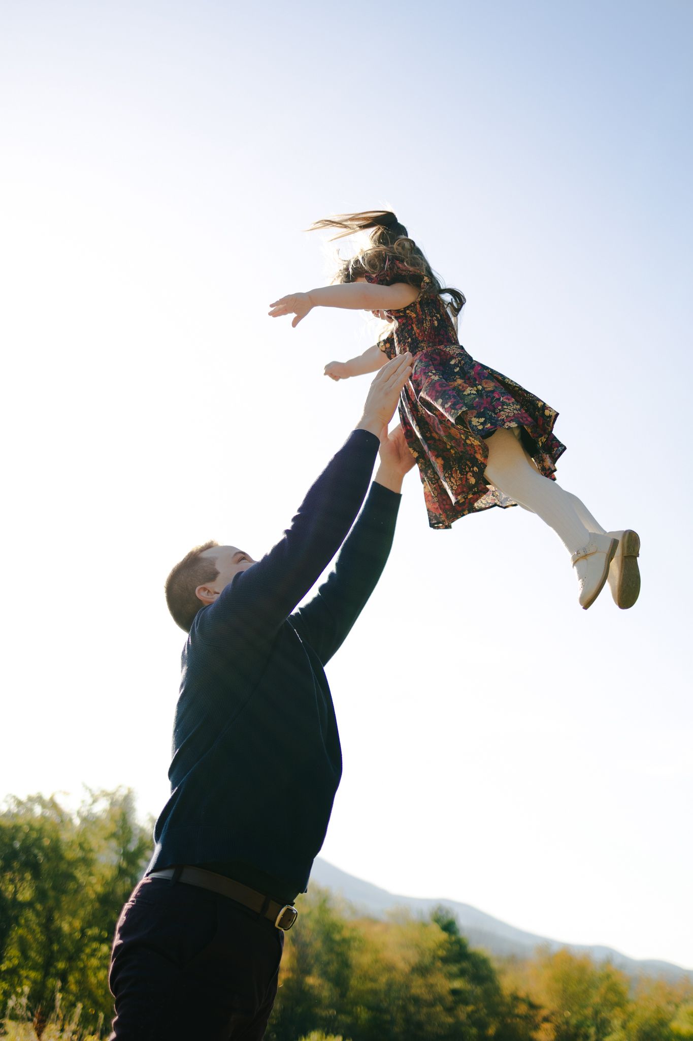 Outdoor image of father throwing young daughter in air