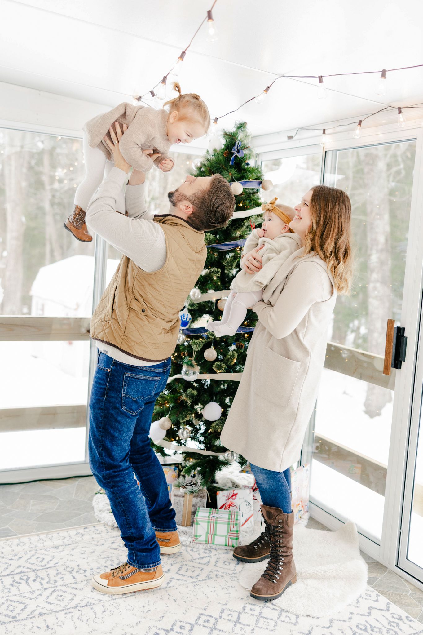 Playful winter scene with people in cream sweaters dancing in front of a decorated Christmas tree.