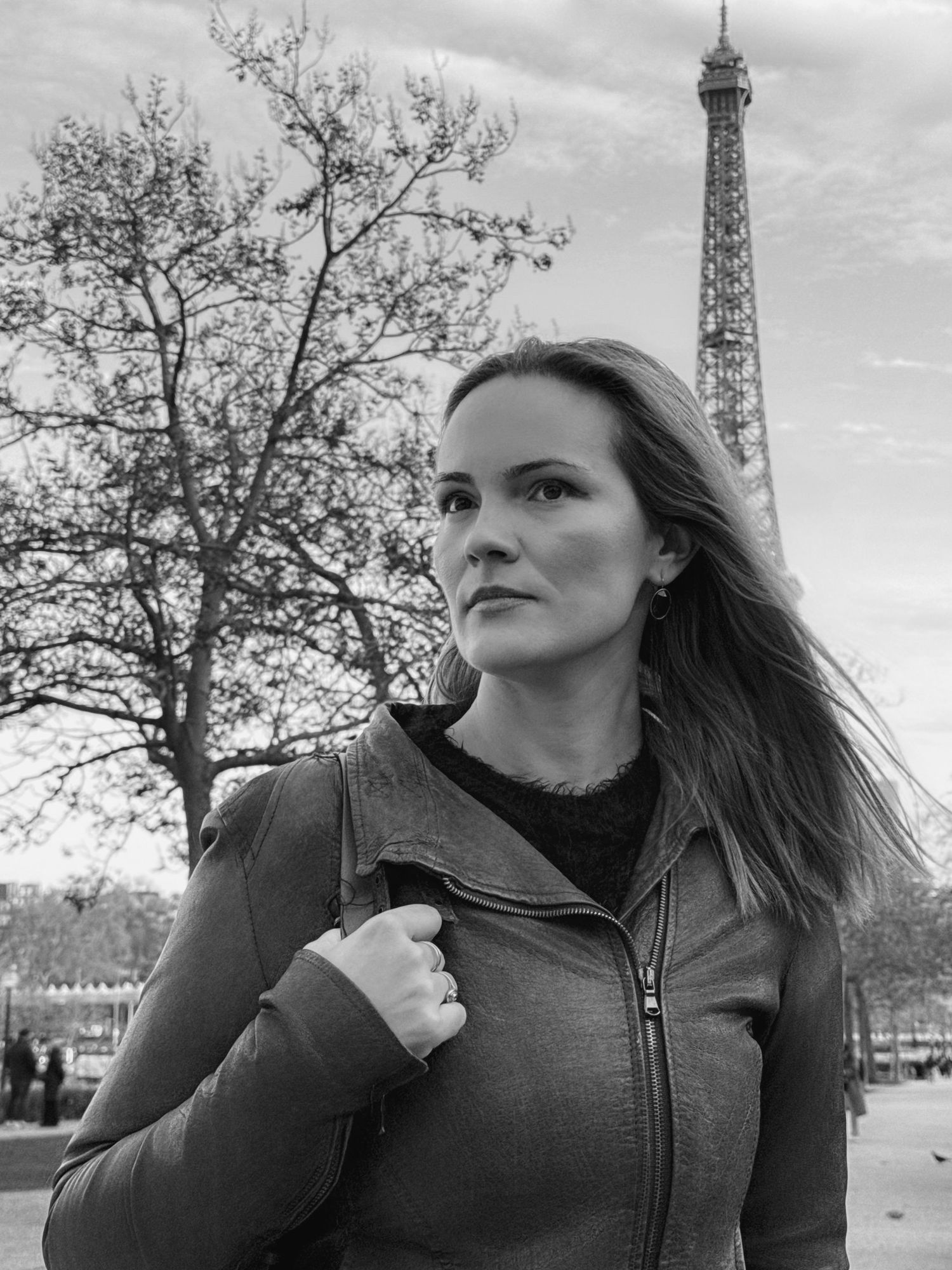 Black and white photo of a woman in a leather jacket posing in front of the Eiffel Tower in Paris.