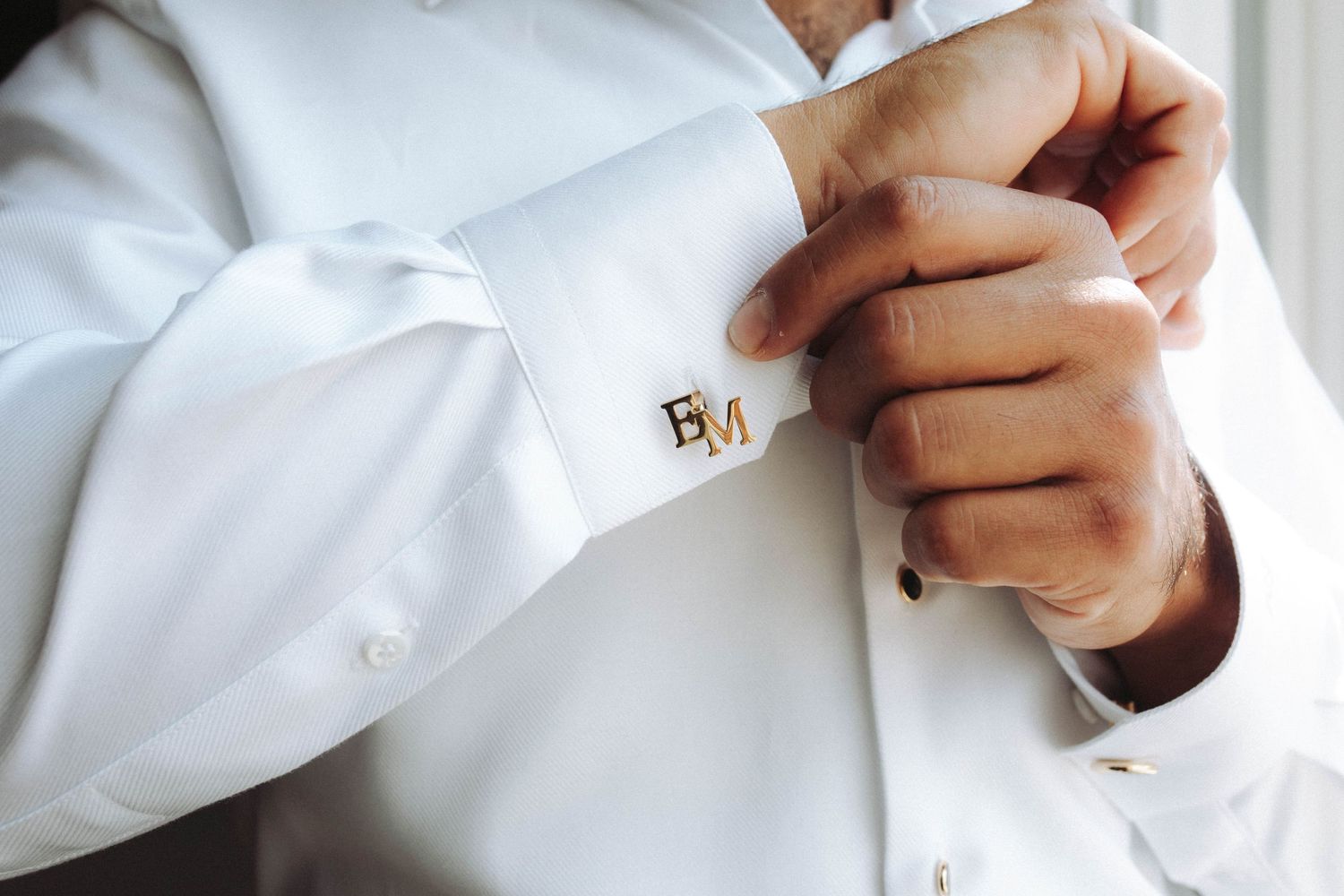 Close-up of hands adjusting gold cufflink on crisp white dress shirt sleeve.