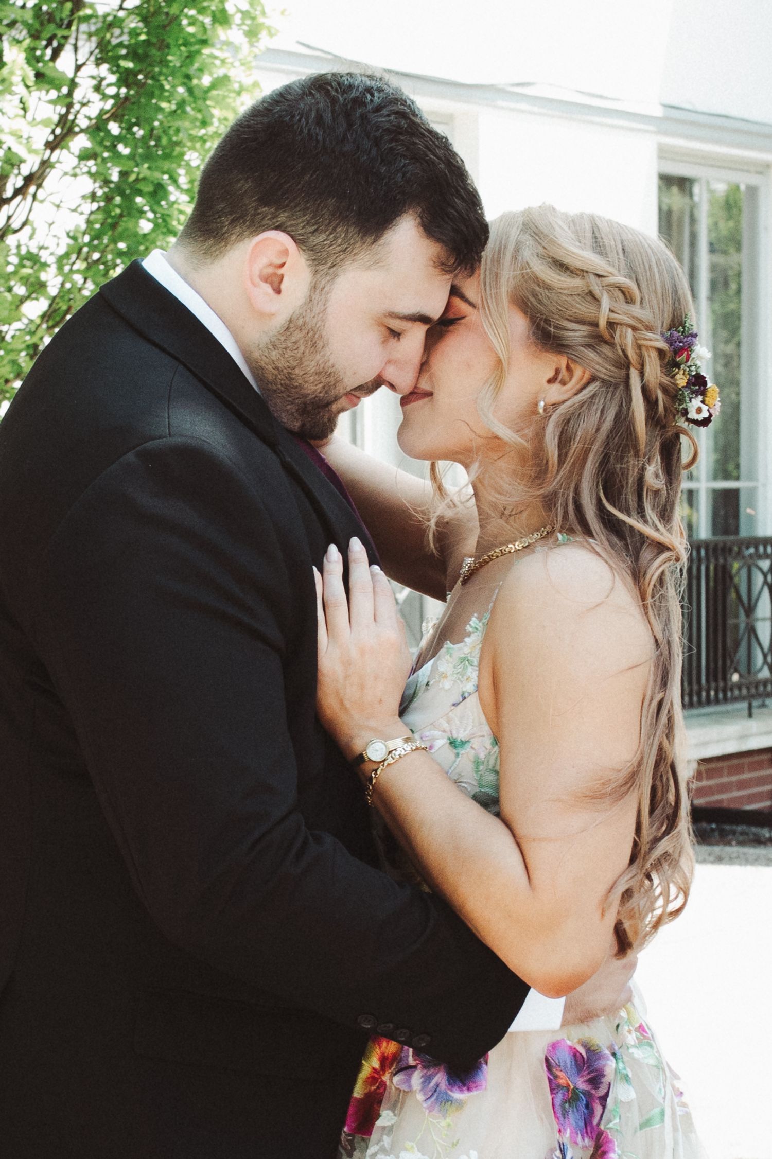 A romantic couple shares tender kisses in a series of intimate outdoor portraits with greenery in the background.
