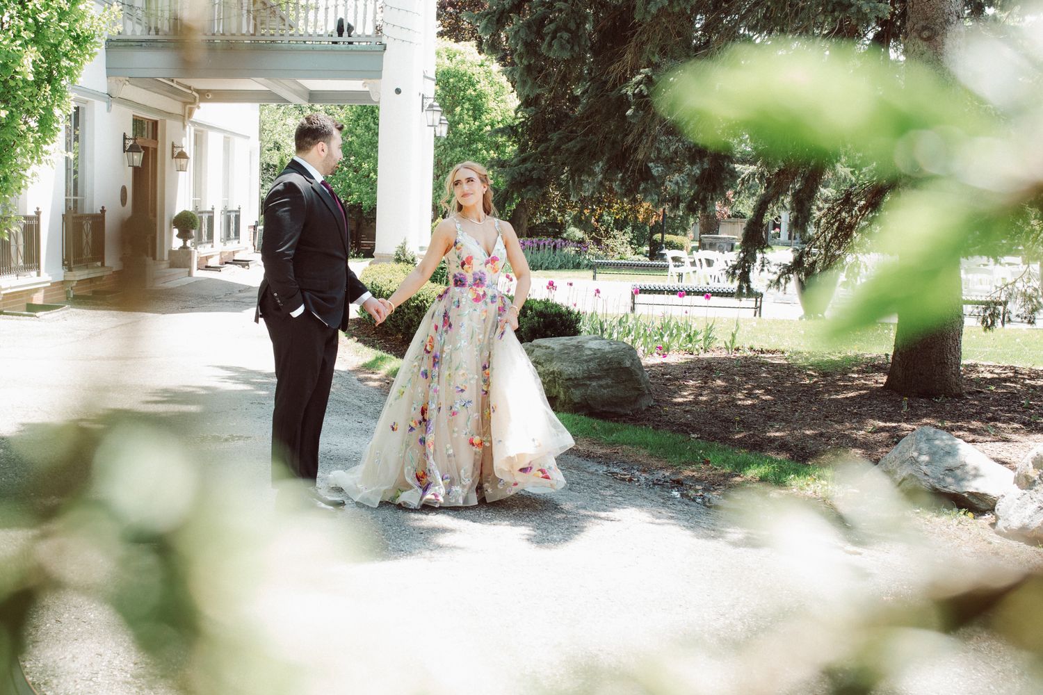 A couple poses together in a garden setting during a wedding celebration outdoors on a sunny day.