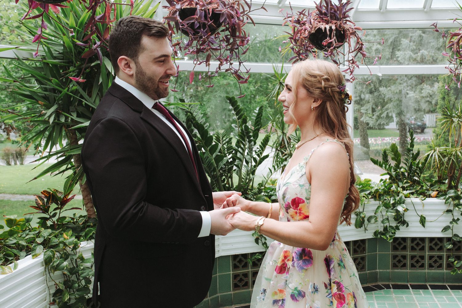 A couple exchanges rings during a romantic wedding ceremony in a lush greenhouse filled with tropical plants.