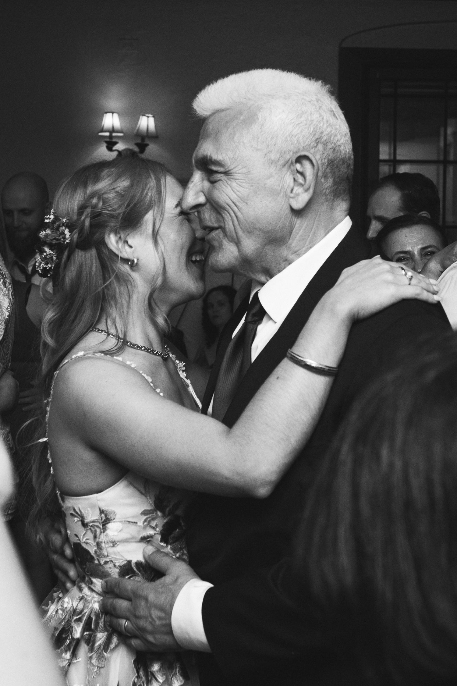 A couple shares an intimate dance and kiss at a formal event in black and white photography.