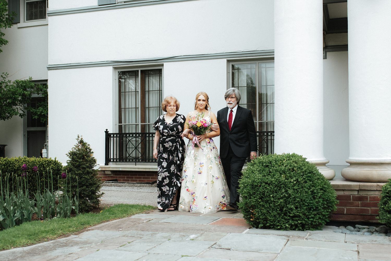 A bride and groom share a tender moment under a white columned portico at an elegant wedding venue.