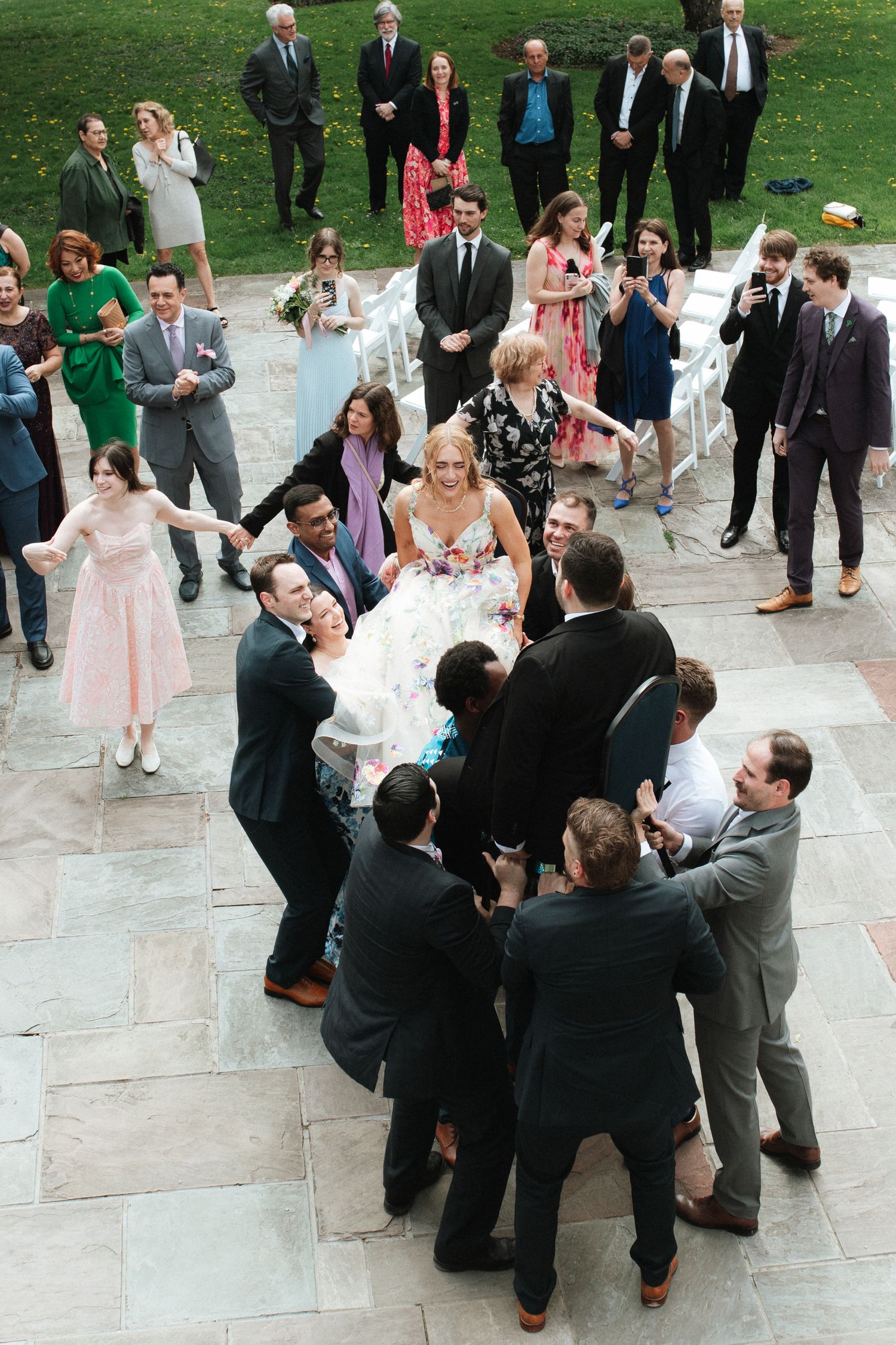 Wedding guests gather on stone patio during outdoor reception celebration in formal attire.