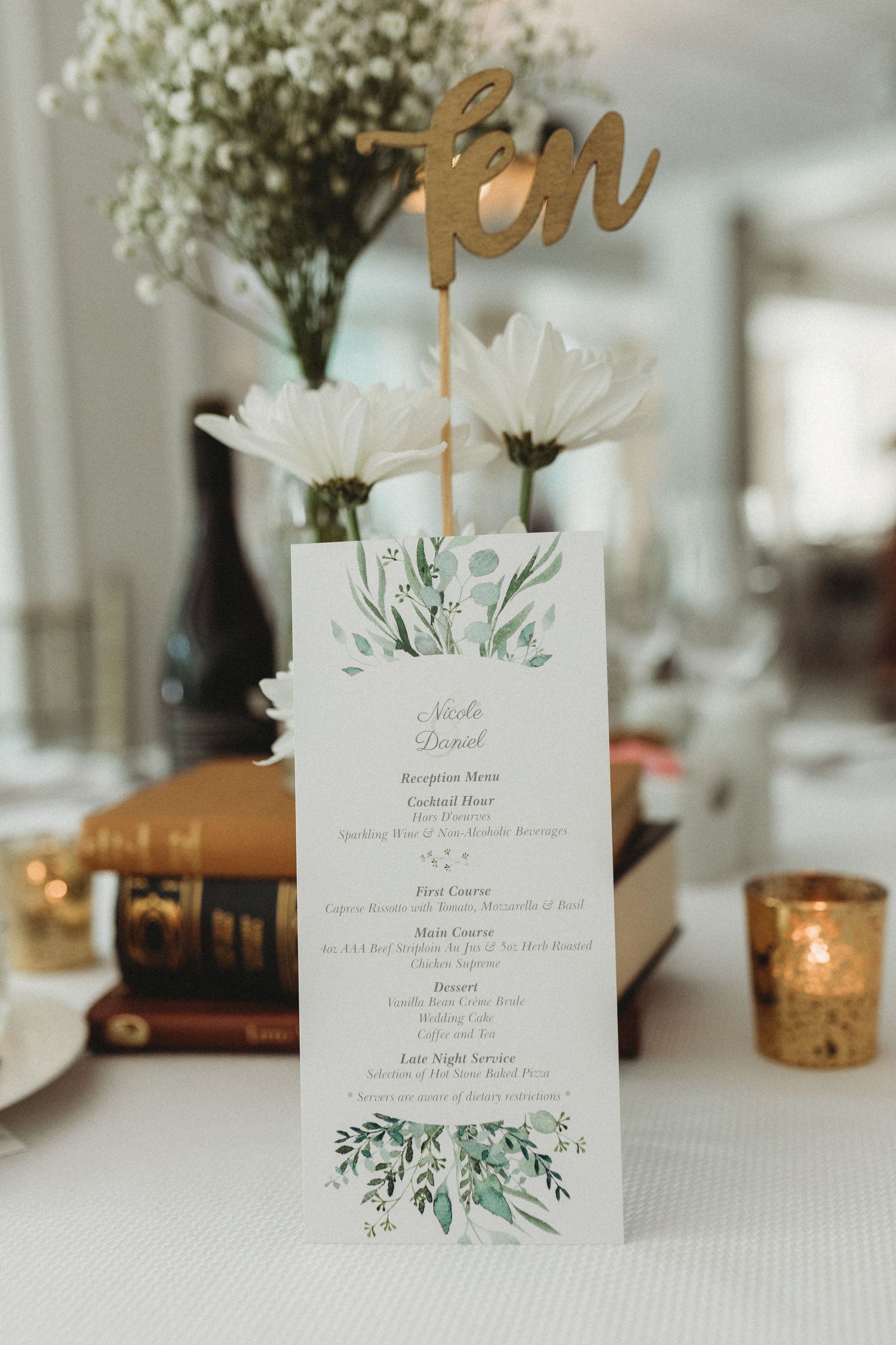 Elegant wedding menu card with gold 'ten' table number and white daisies in a vase, decorated with greenery watercolor details.