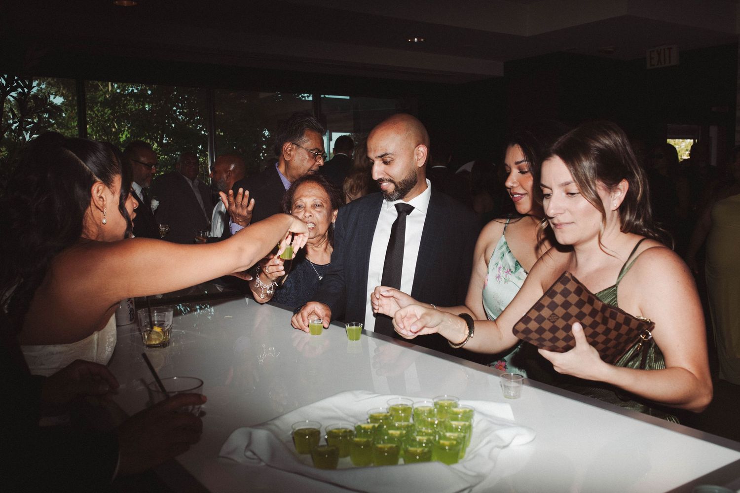 Wedding guests enjoy taking shots at a reception party with green drinks lined up on the bar.