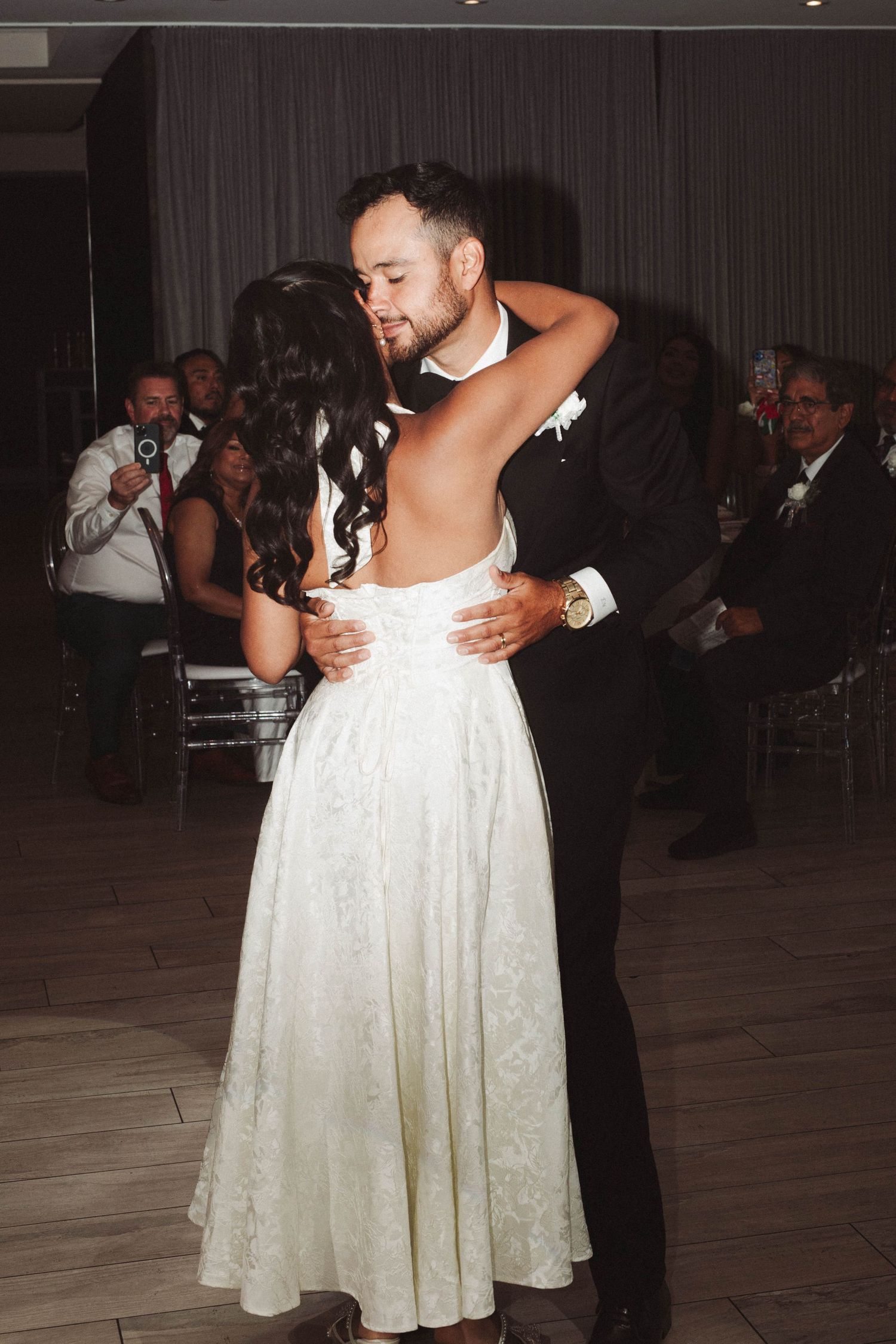 A couple shares an intimate dance moment at a wedding reception on a wooden dance floor.
